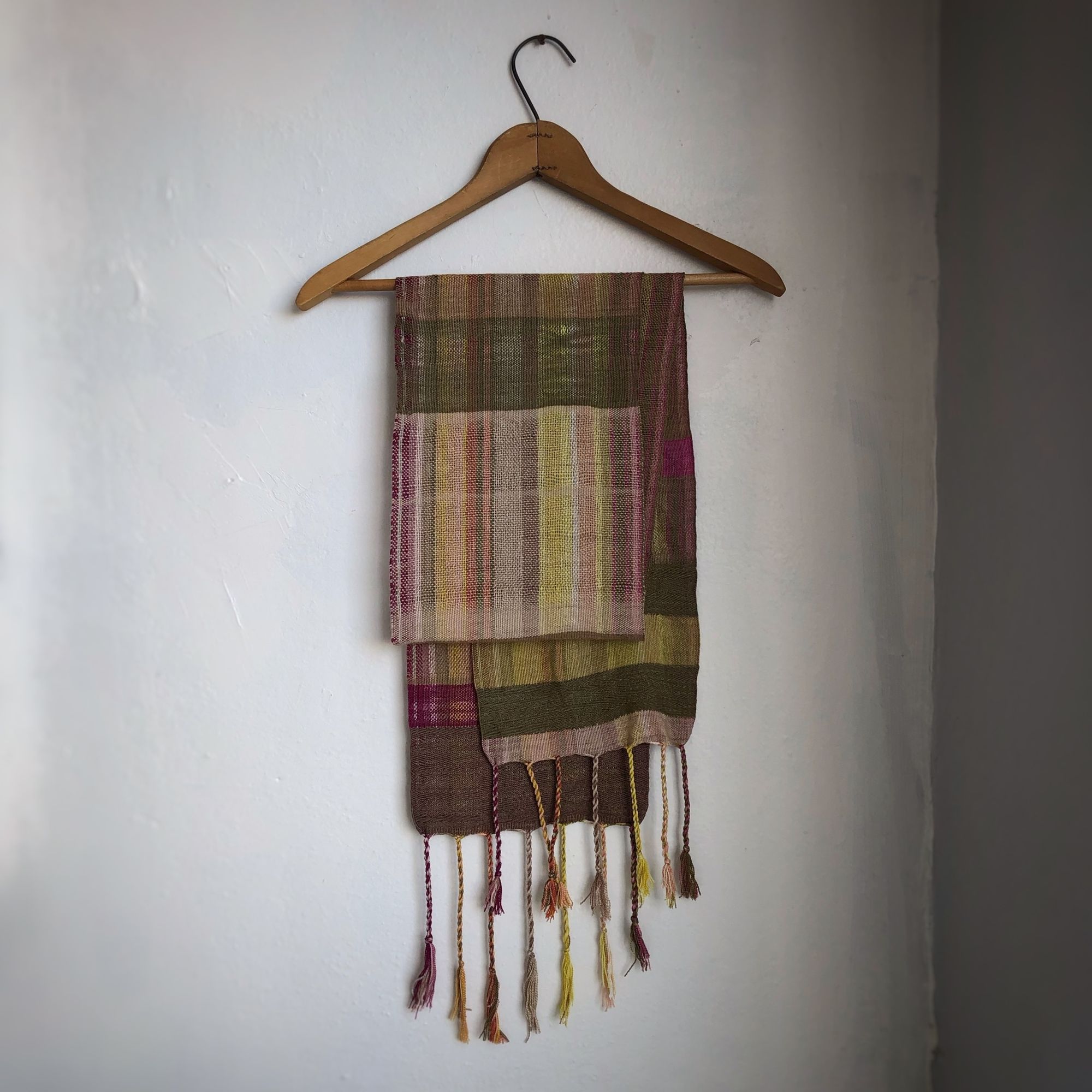 Naturally dyed earth-tone scarf hanging on a hanger on a white wall