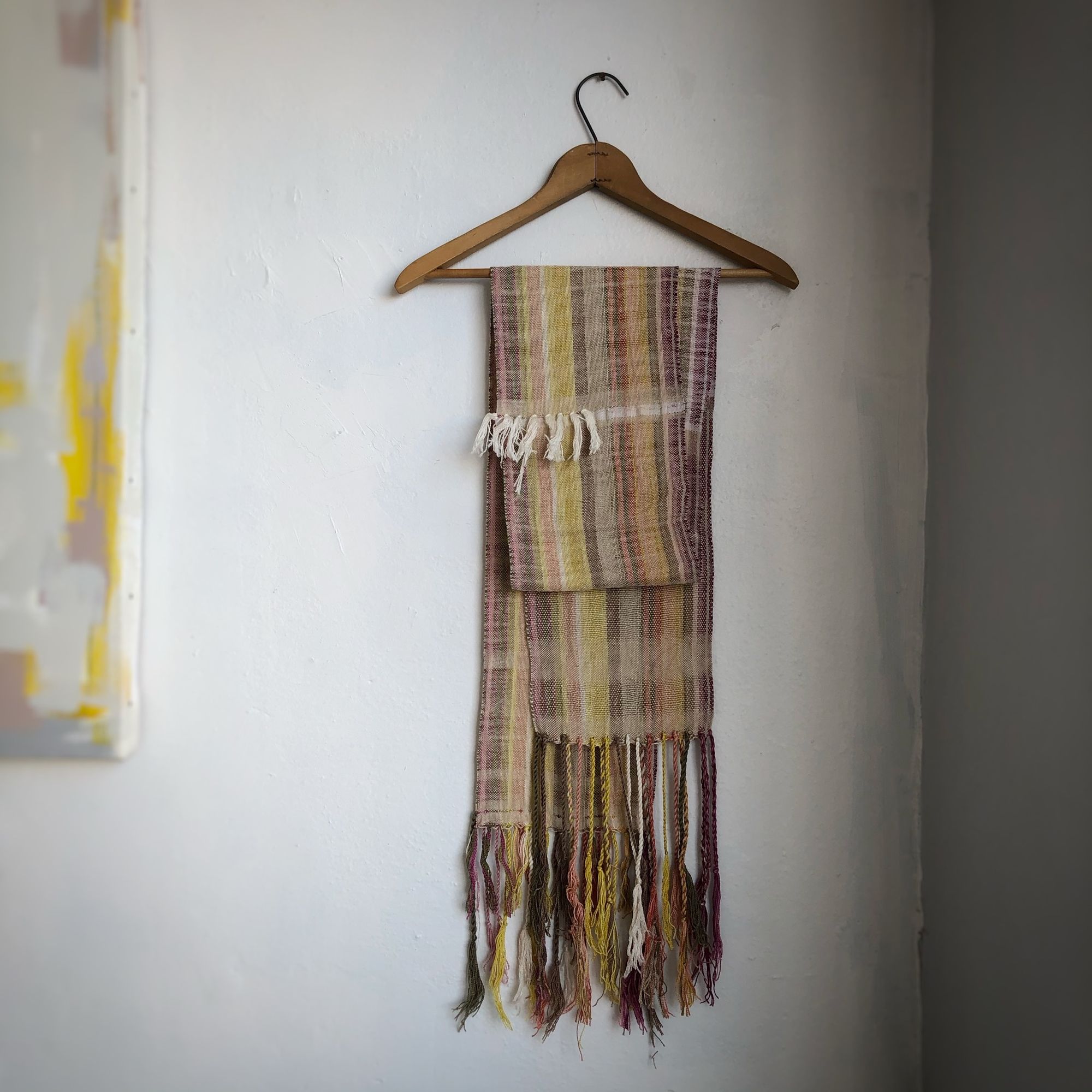 Naturally dyed earth-tone scarf hanging on a hanger on a white wall