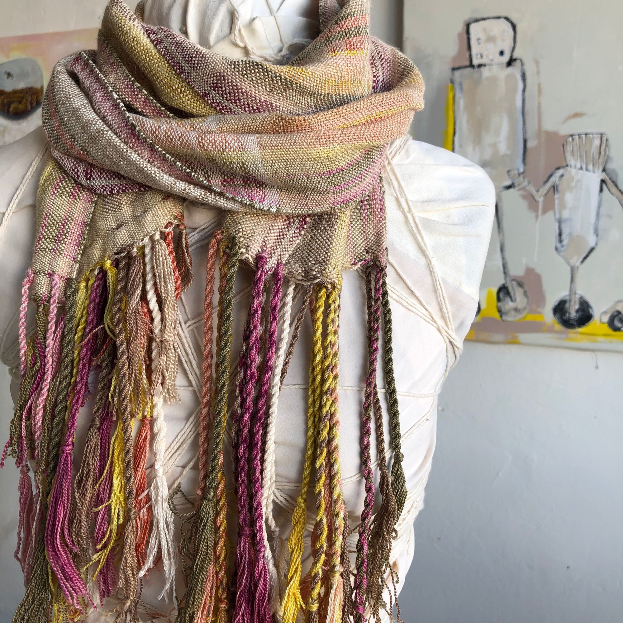 naturally colored scarf on a white mannequin in a gallery with paintings in the background