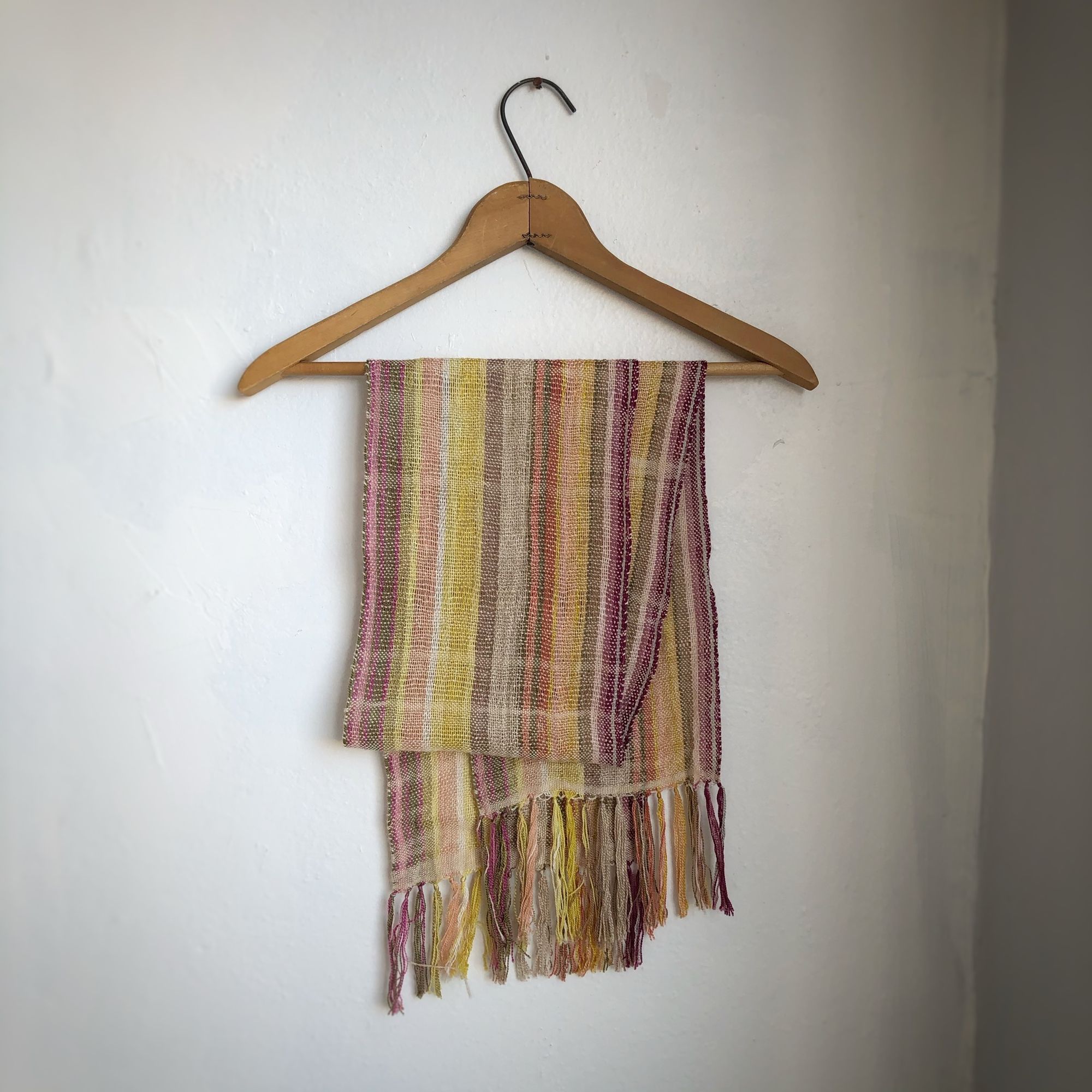 Naturally dyed earth-tone scarf hanging on a hanger on a white wall