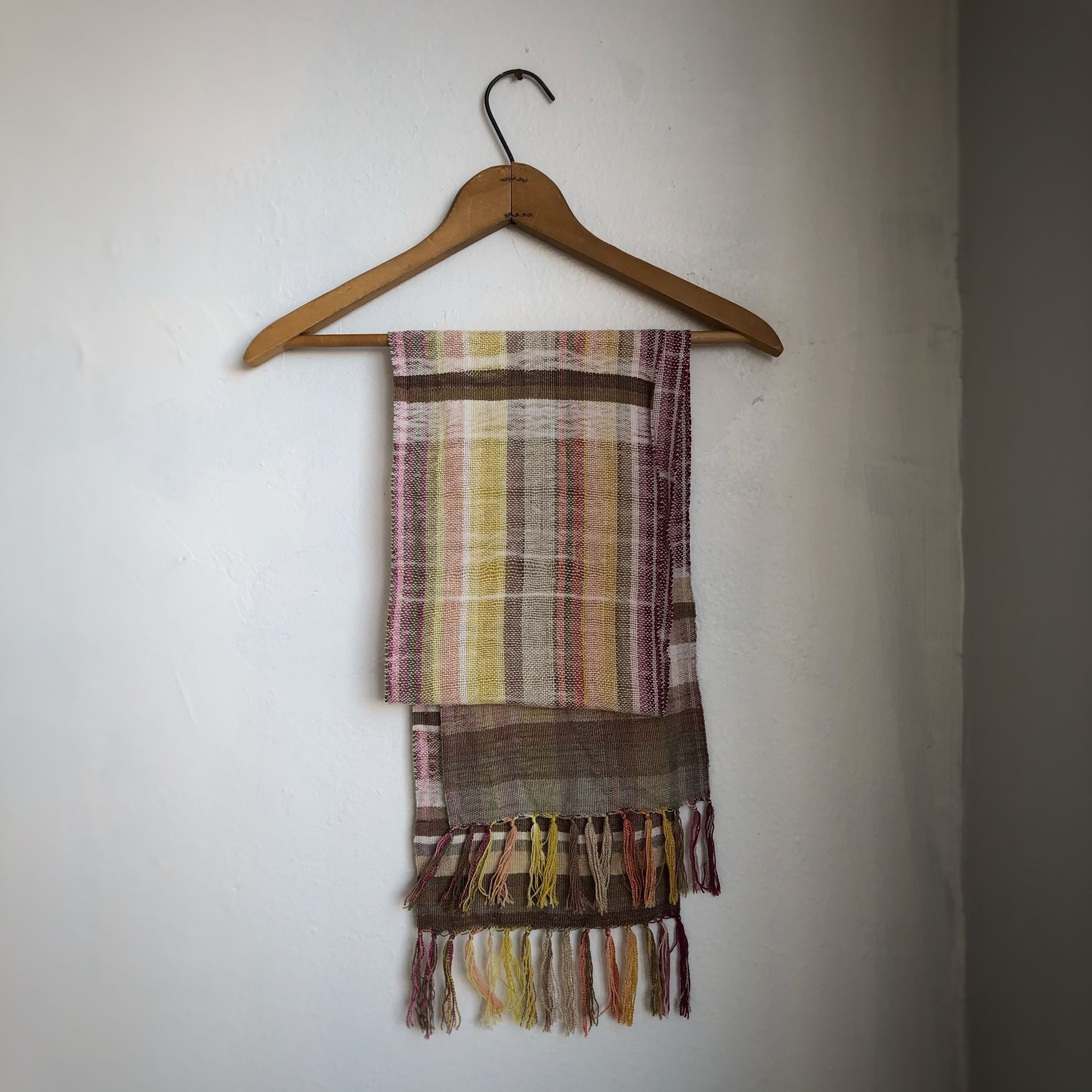 Naturally dyed earth-tone scarf hanging on a hanger on a white wall