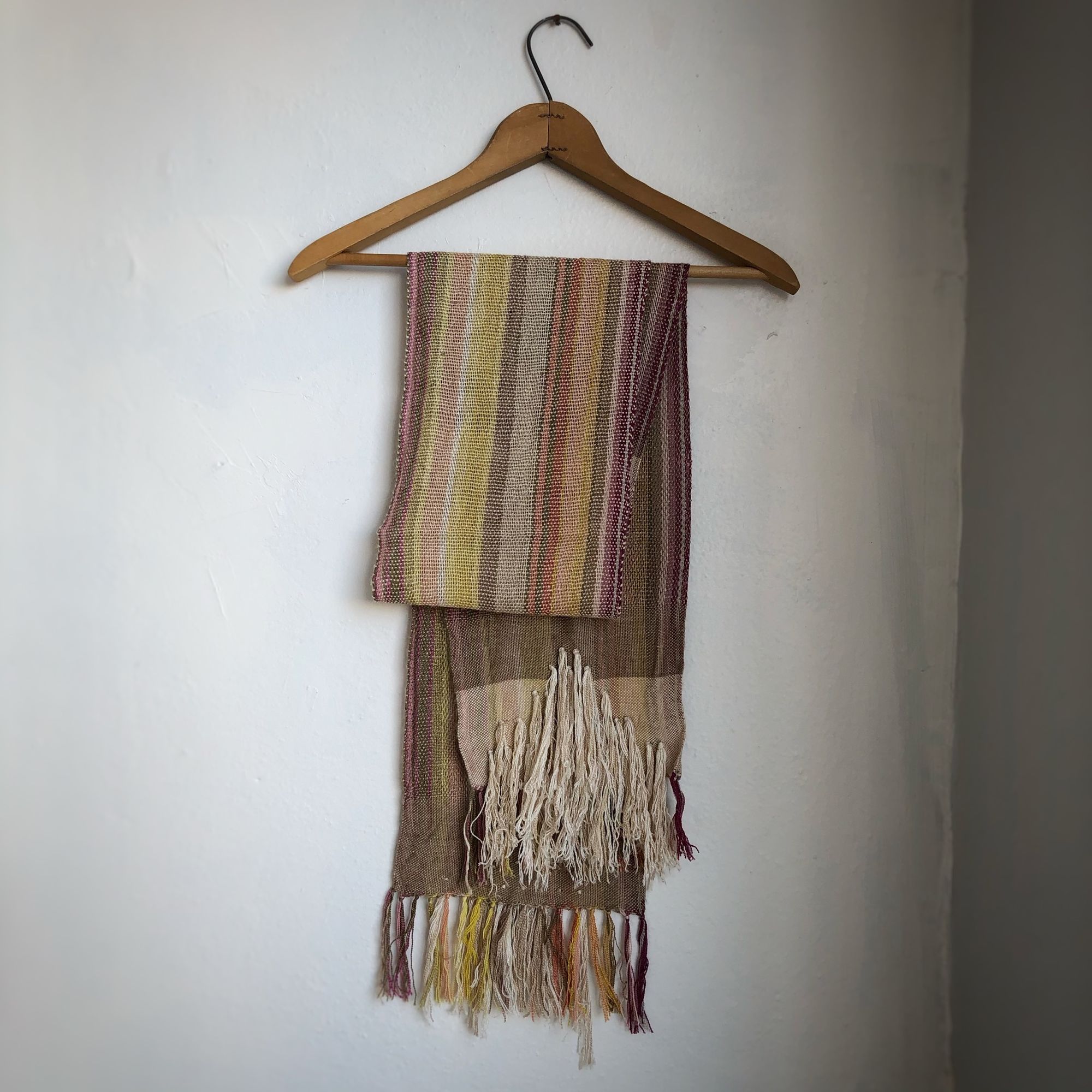 Naturally dyed earth-tone scarf hanging on a hanger on a white wall