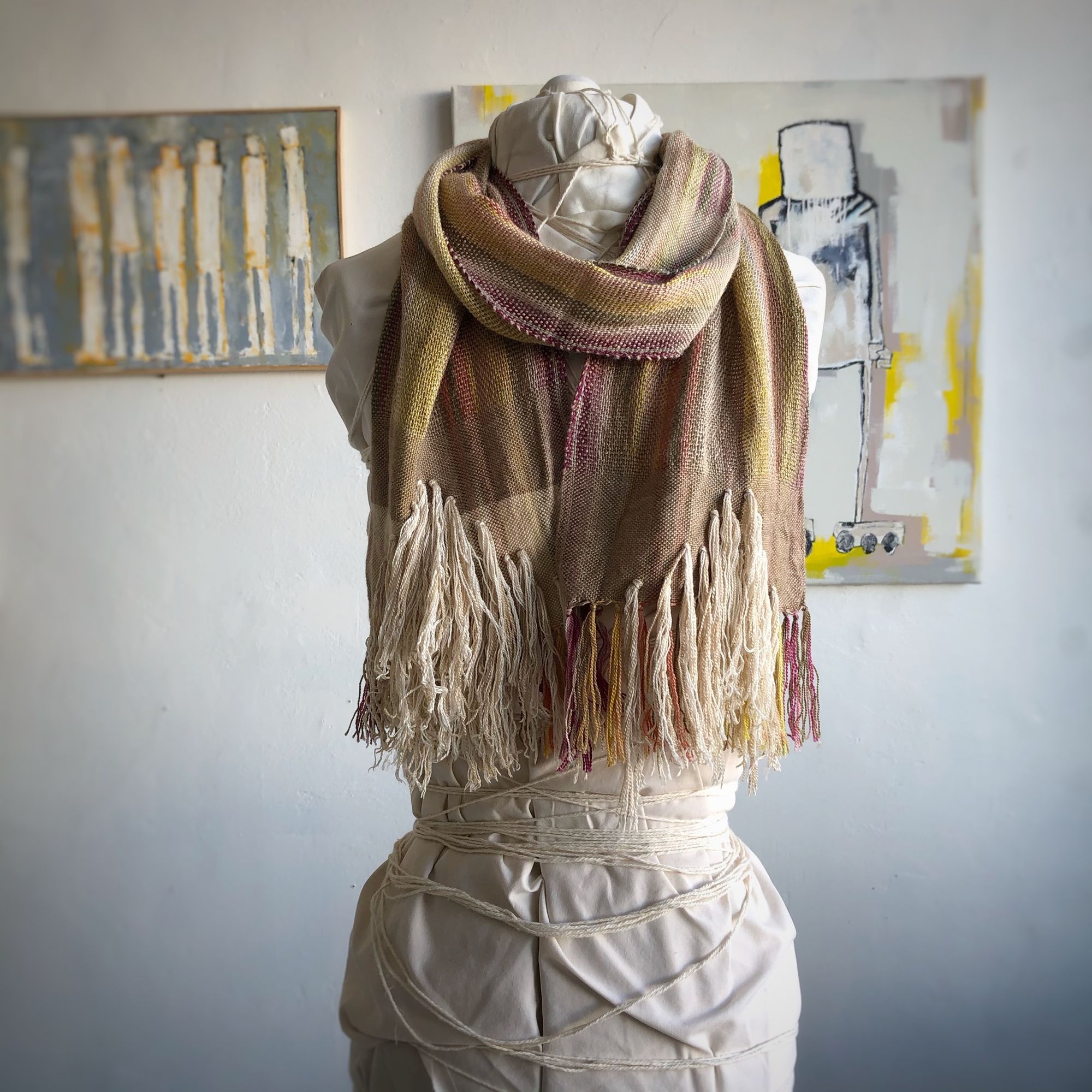 naturally colored scarf on a white mannequin in a gallery with paintings in the background