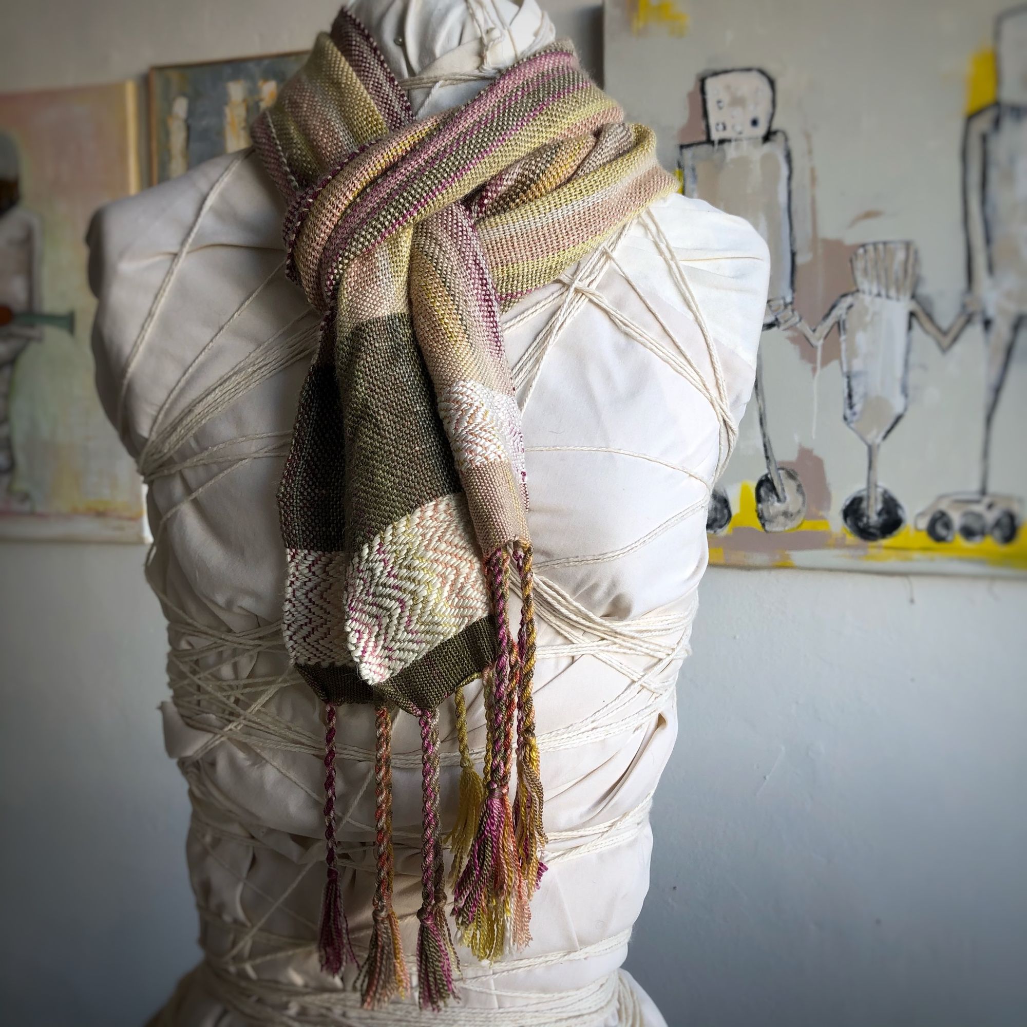 naturally colored scarf on a white mannequin in a gallery with paintings in the background