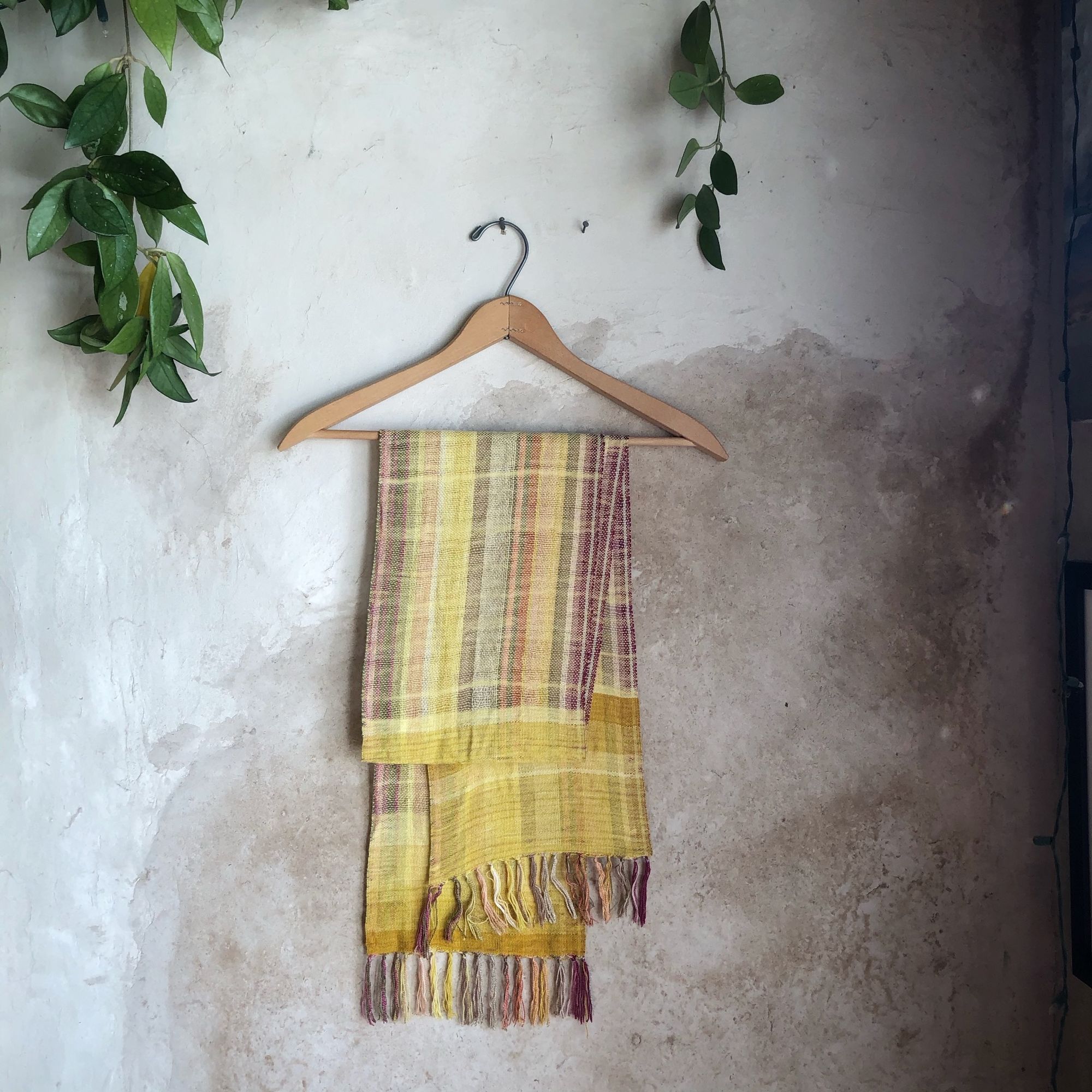 Naturally dyed earth-tone scarf hanging on a hanger on a white wall