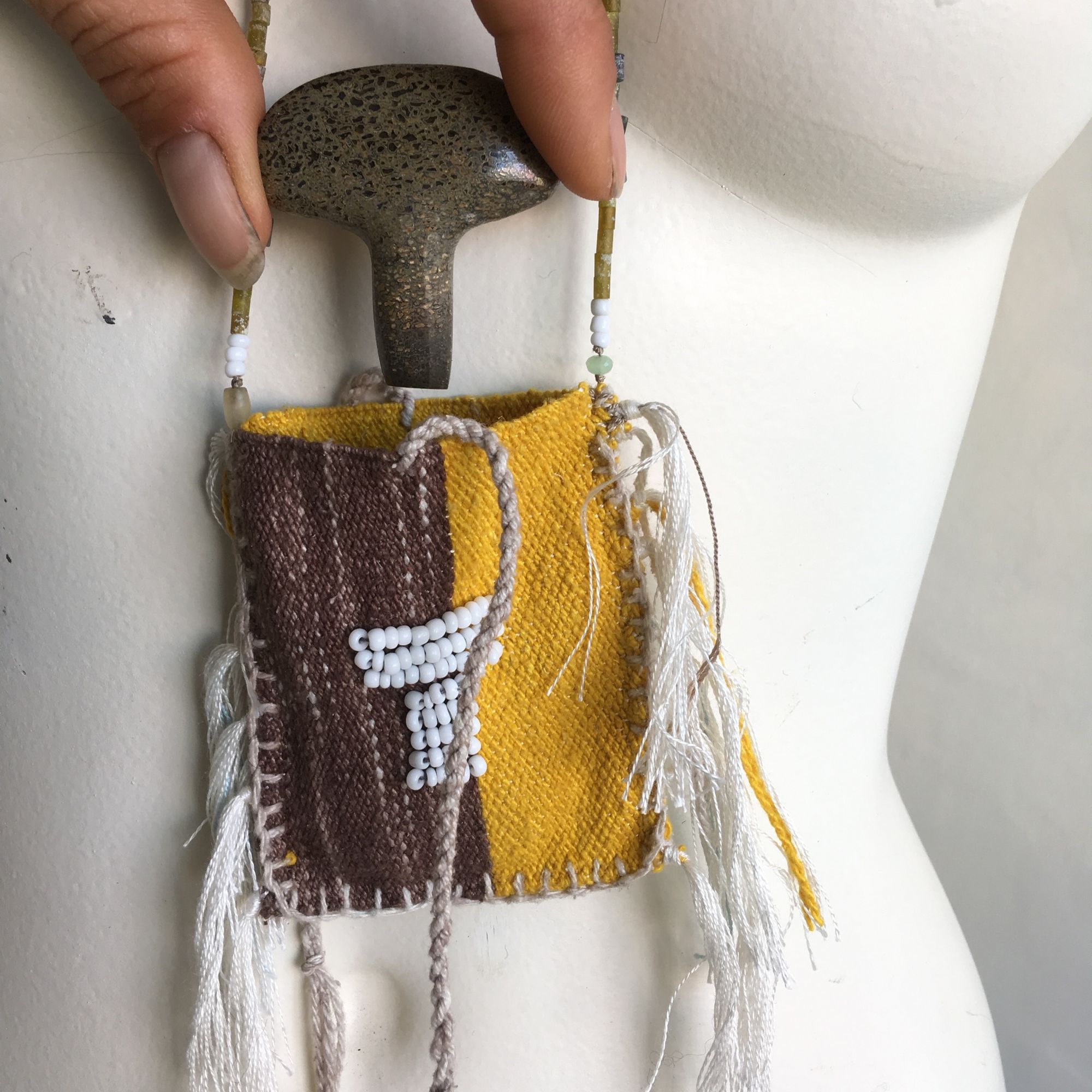 detail of yellow brown and green beaded necklace with a brown and yellow woven pouch with white beadwork on a white mannequin