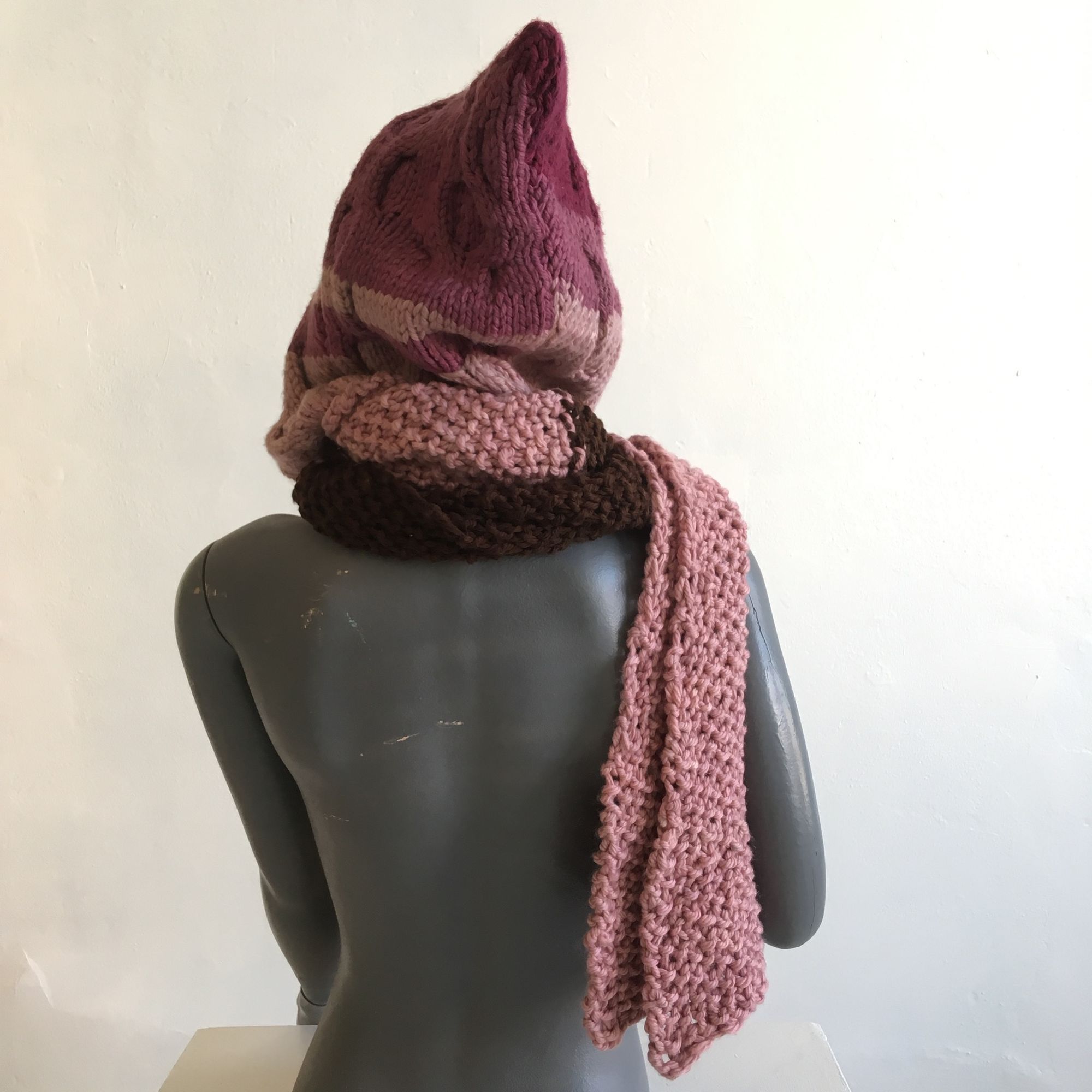 pink and brown cable knit hood-scarf on a grey mannequin against a white wall