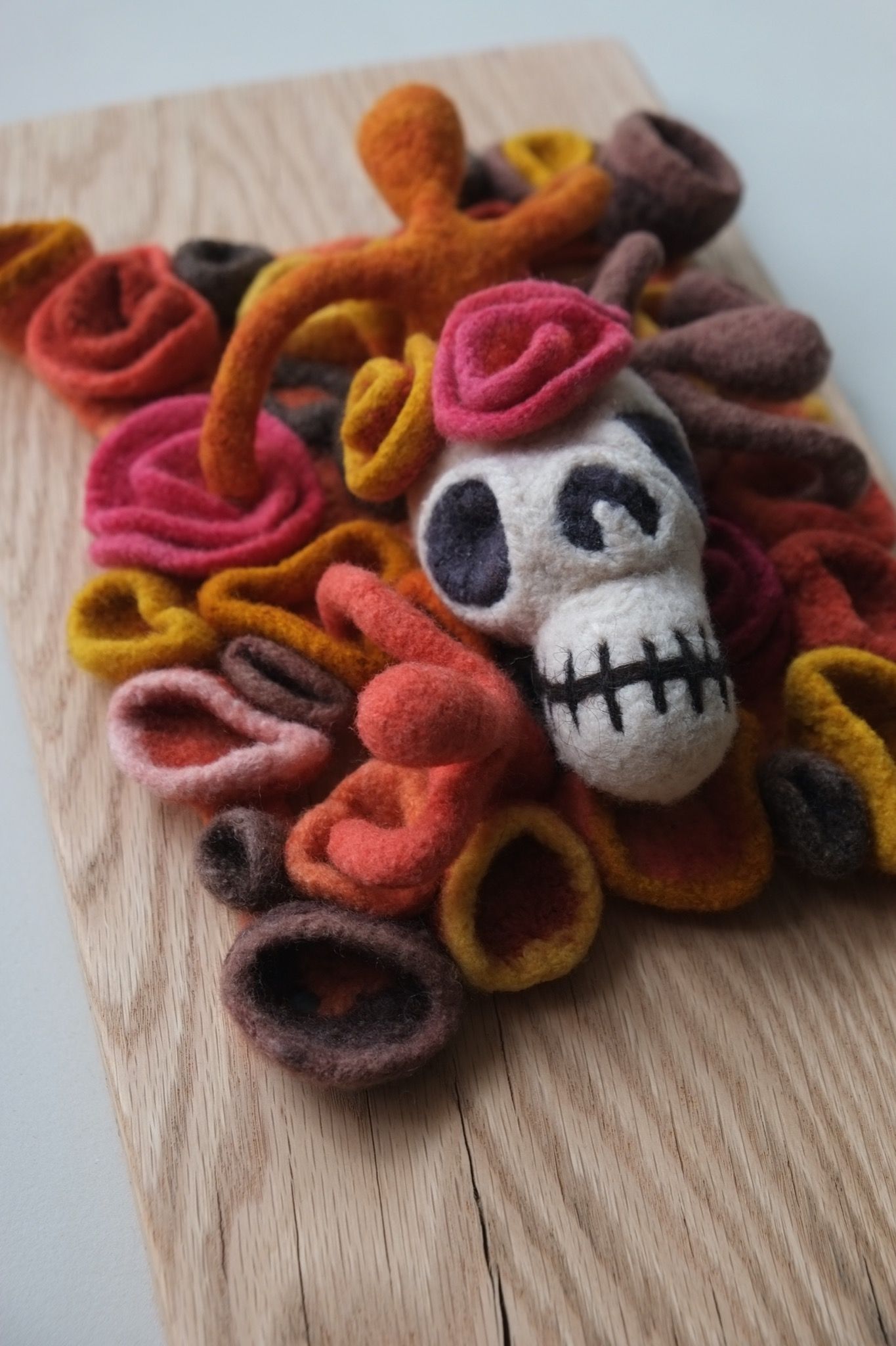 wall sculpture with a skull, floral and human forms in multicolored felt coming out of an oak plank