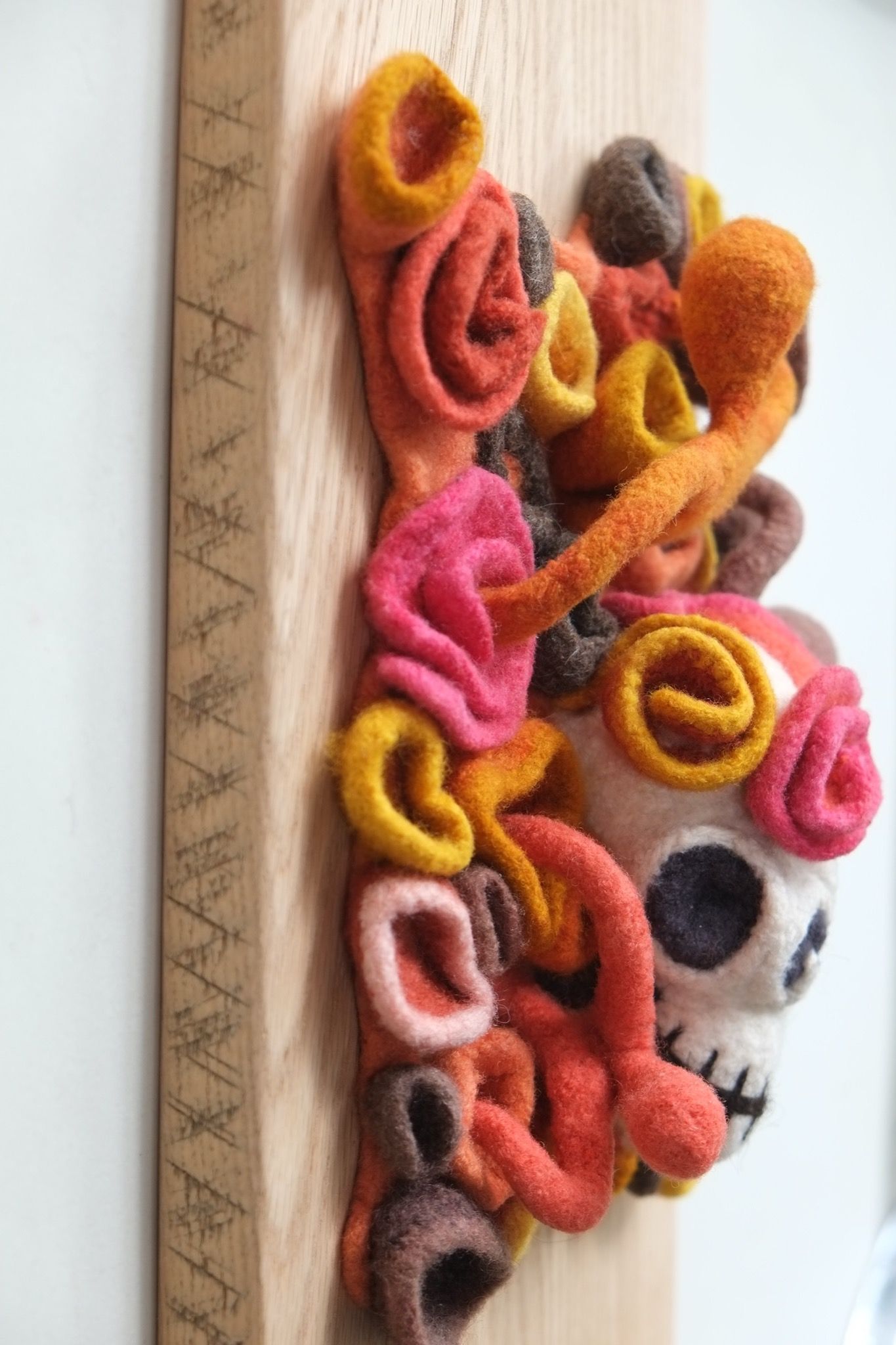 wall sculpture with a skull, floral and human forms in multicolored felt coming out of an oak plank