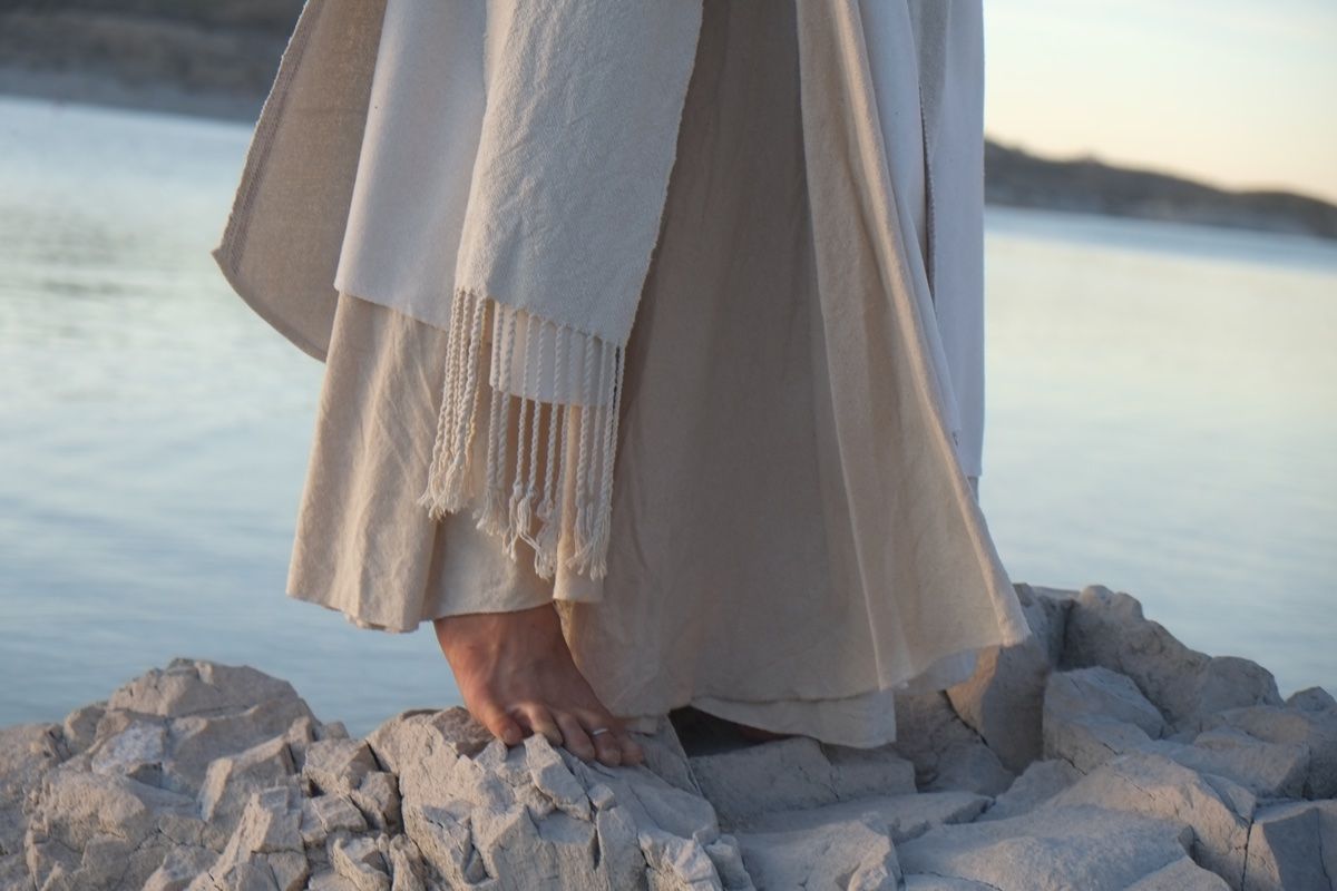 woman wearing white wedding skirt and lilac shirt by a still lake at sunset