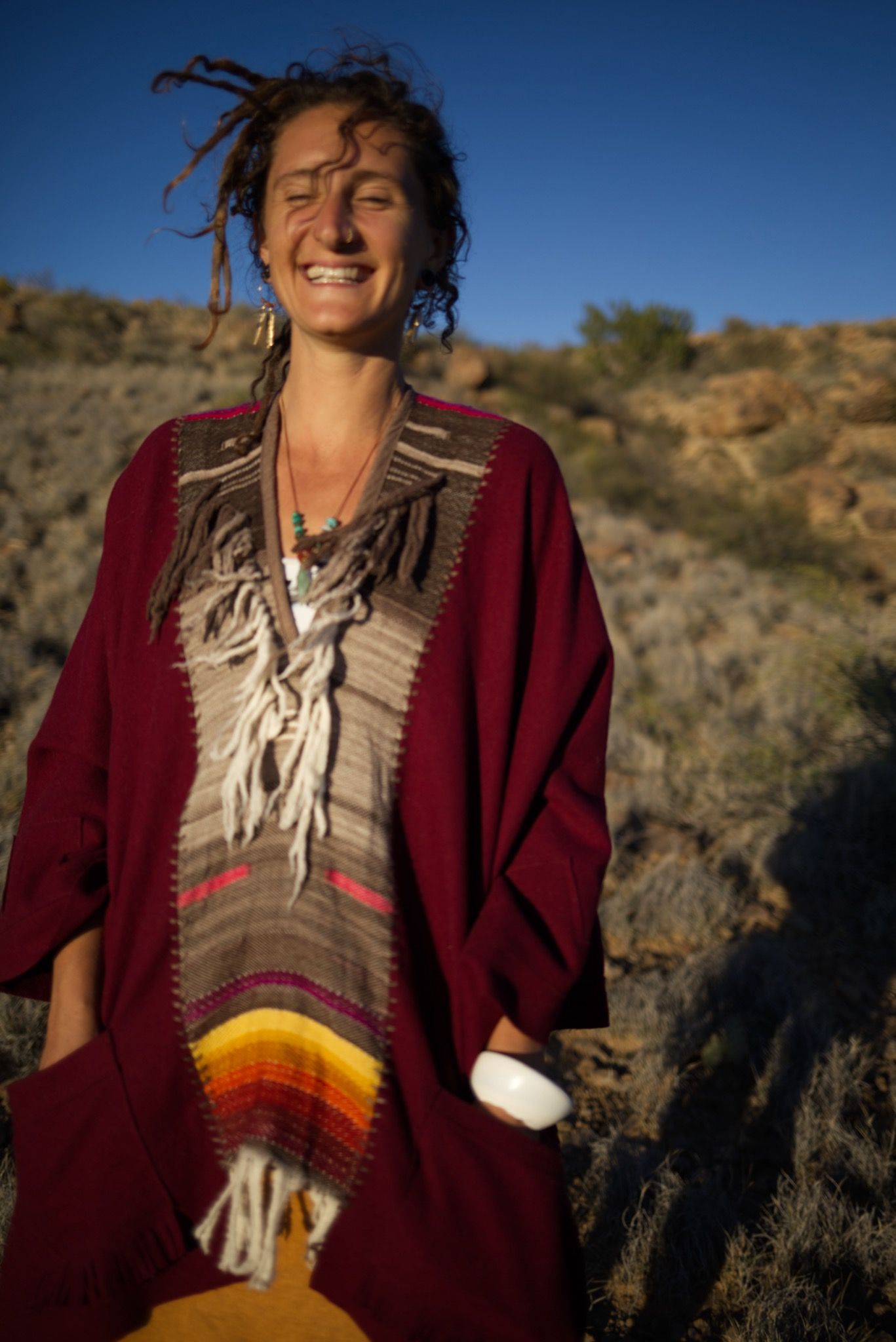 woman wearing a red, brown and rainbow cloak in the desert on a blue sky day