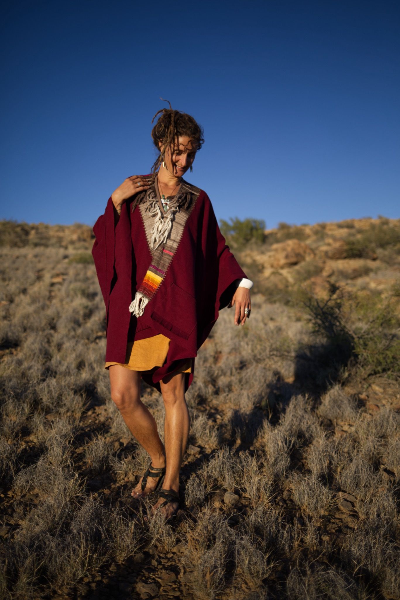 woman wearing a red, brown and rainbow cloak in the desert on a blue sky day