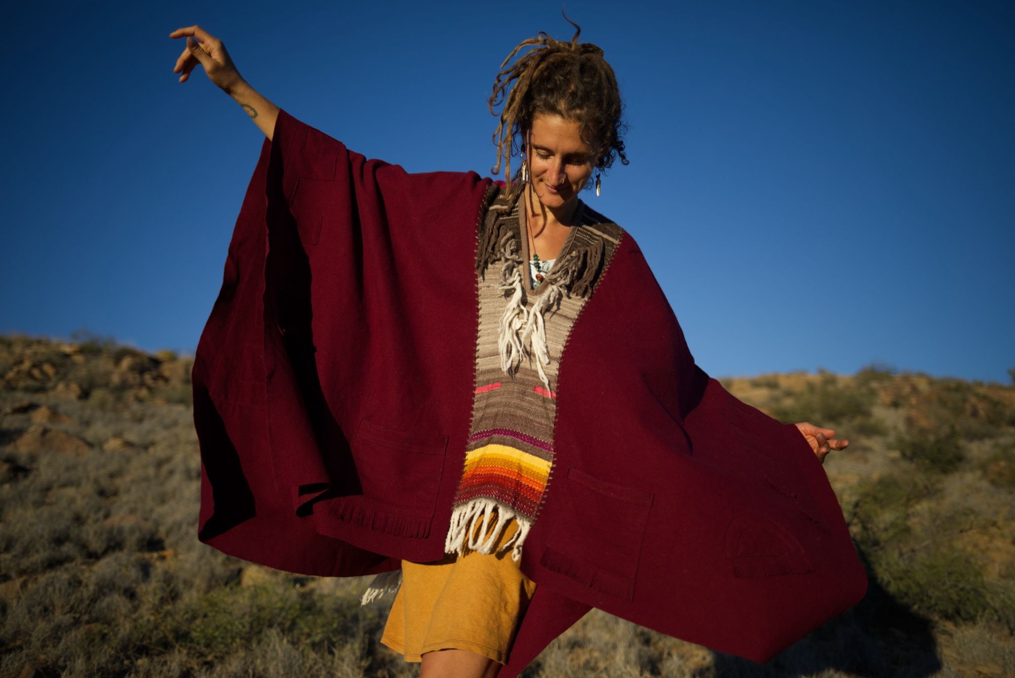 woman wearing a red, brown and rainbow cloak in the desert on a blue sky day