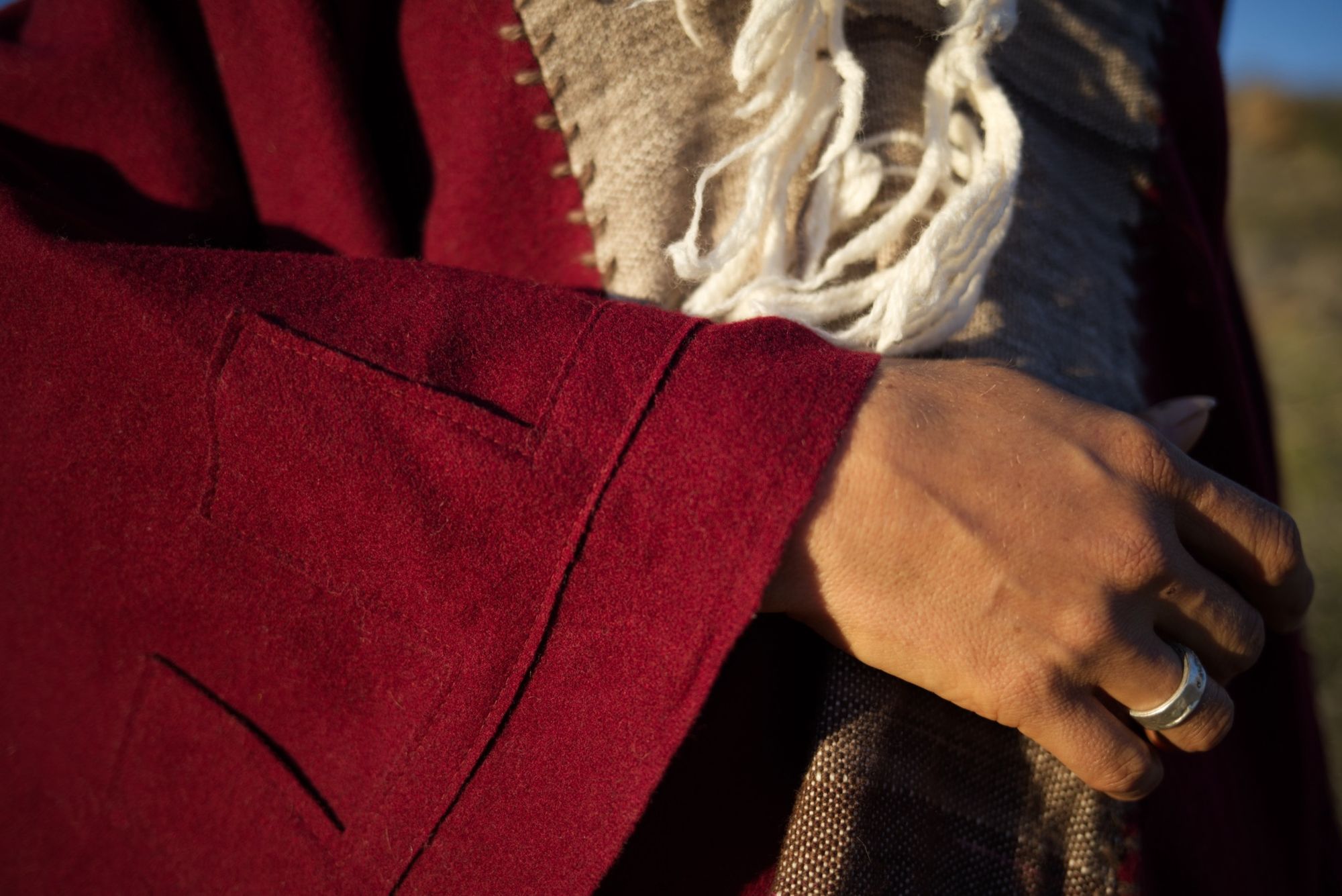 woman wearing a red, brown and rainbow cloak in the desert on a blue sky day