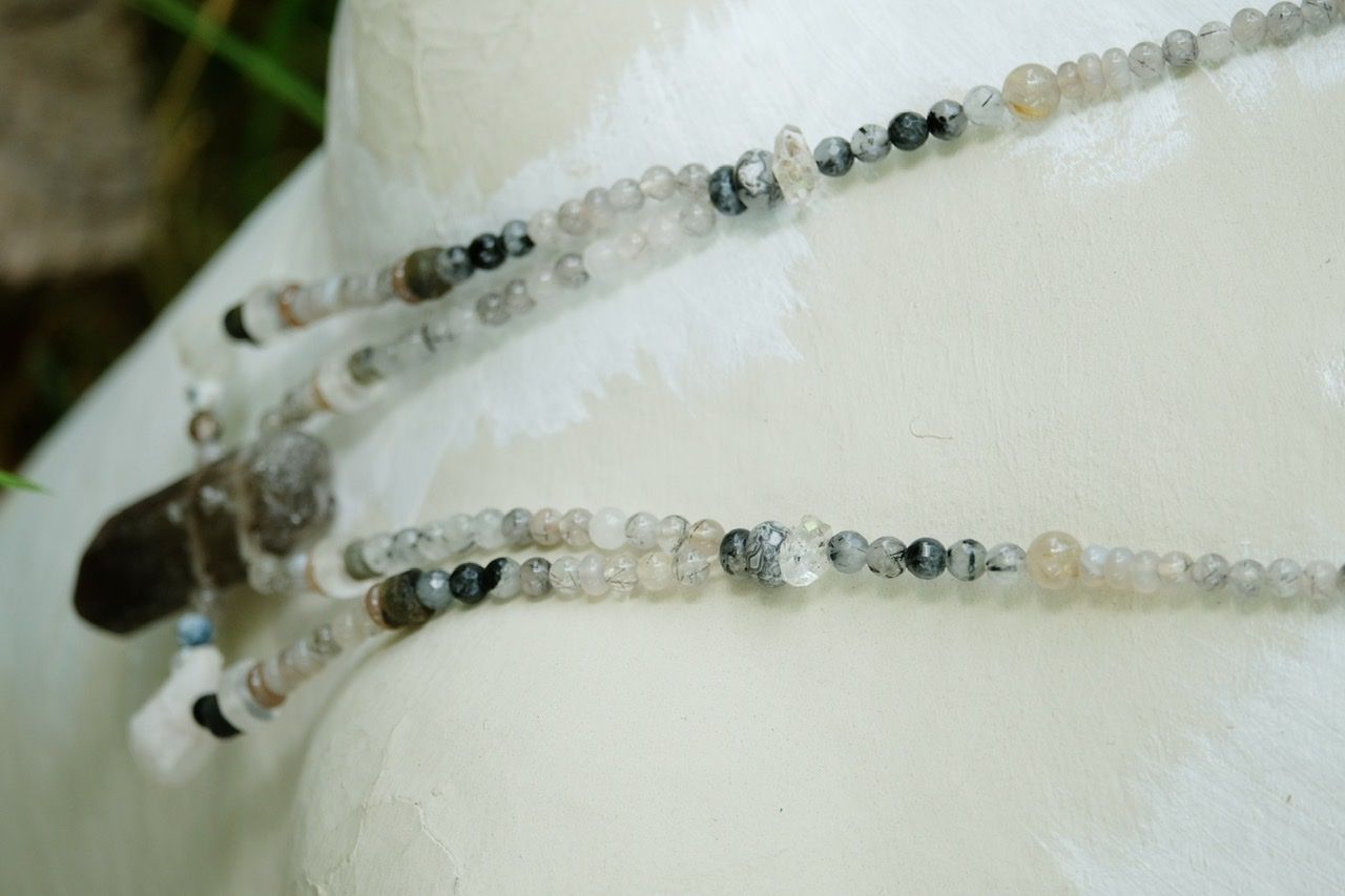 grey smoky quartz and clear crystal stone necklace on a white mannequin surrounded by green plants