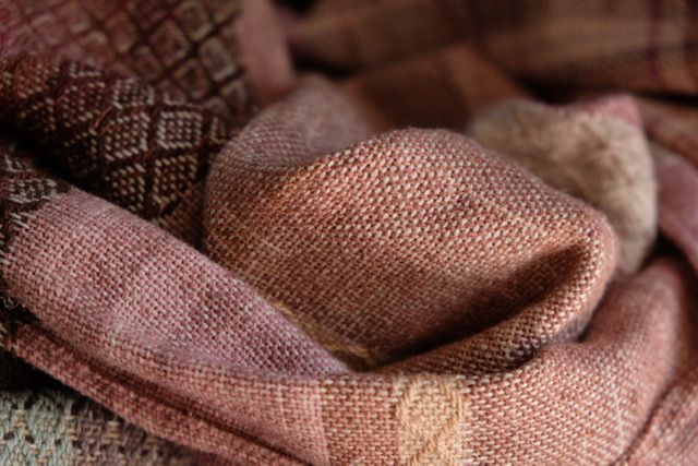 Handwoven fabric with a textured diamond pattern in pinks, blues, white and earth tones, laying on a wooden floor