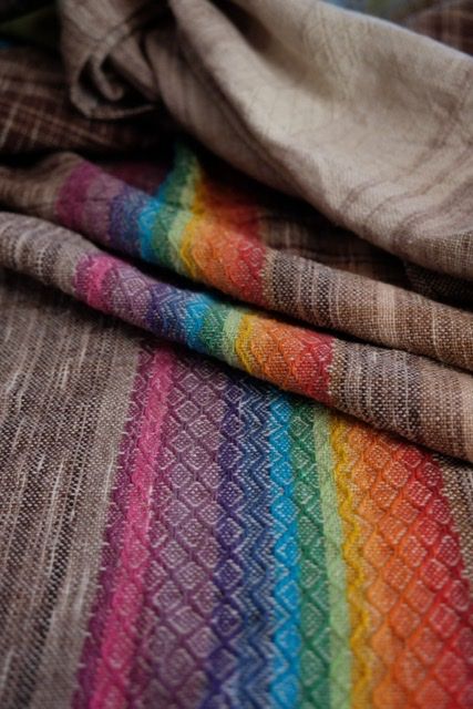 Handwoven fabric with diamond pattern in browns and all the colors of the rainbow, on a wooden floor
