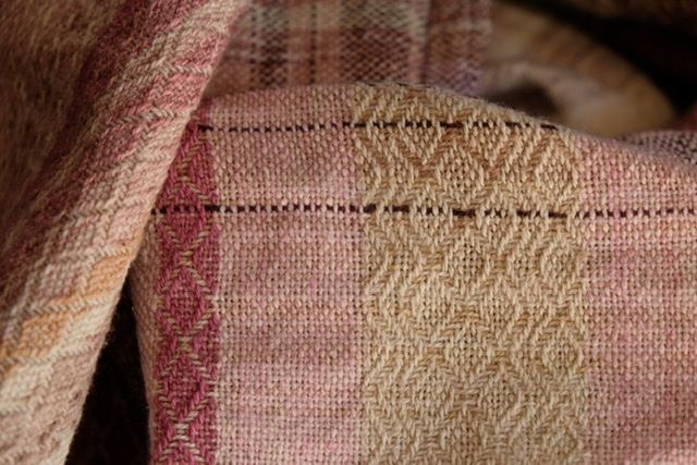 Handwoven fabric with a textured diamond pattern in pinks, blues, white and earth tones, laying on a wooden floor