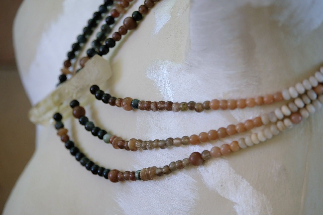 A white female form mannequin wears a three strand black, pink and white necklace with a large citrine point at the center
