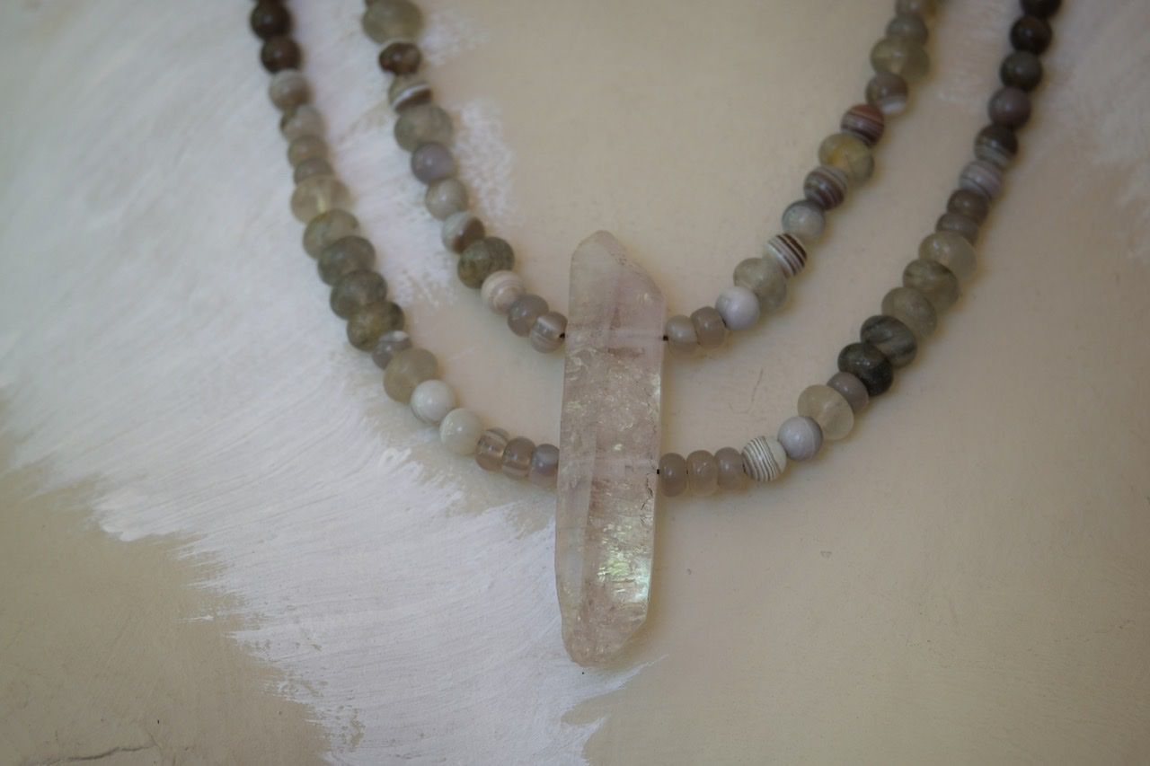 A white female shaped mannequin wearing a necklace made of light purple amethyst and grey White quartz 