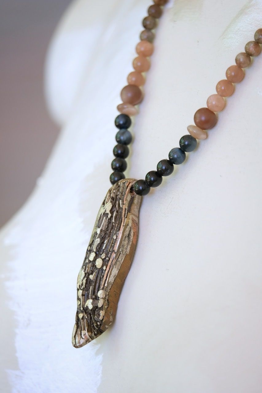 A white female form mannequin wears a necklace with a silver, copper and brass mokume pendant and stone beads of black and pale pink