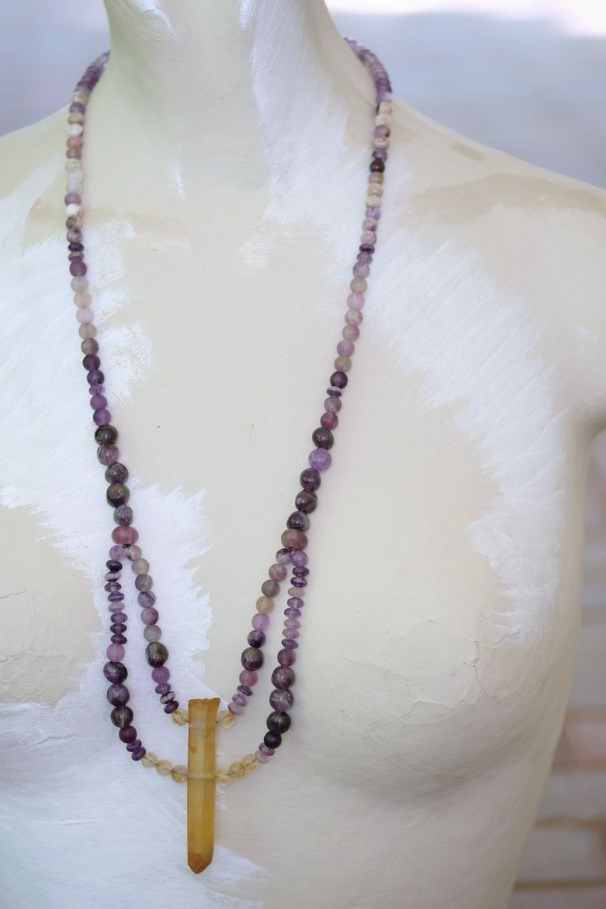 A white mannequin wears a purple and golden yellow stone necklace 