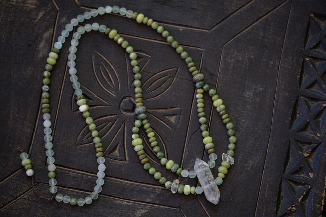  a crystal and green stone necklace on a black wood surface 