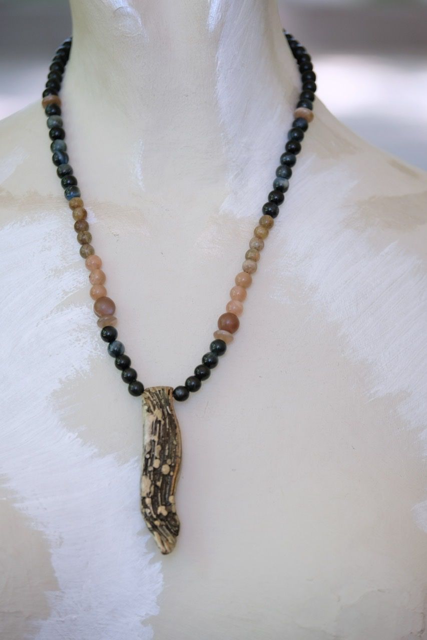A white female form mannequin wears a necklace with a silver, copper and brass mokume pendant and stone beads of black and pale pink