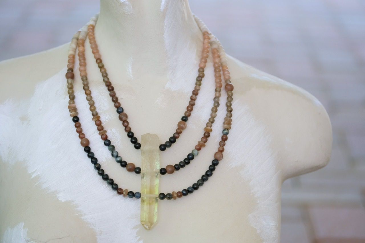 A white female form mannequin wears a three strand black, pink and white necklace with a large citrine point at the center