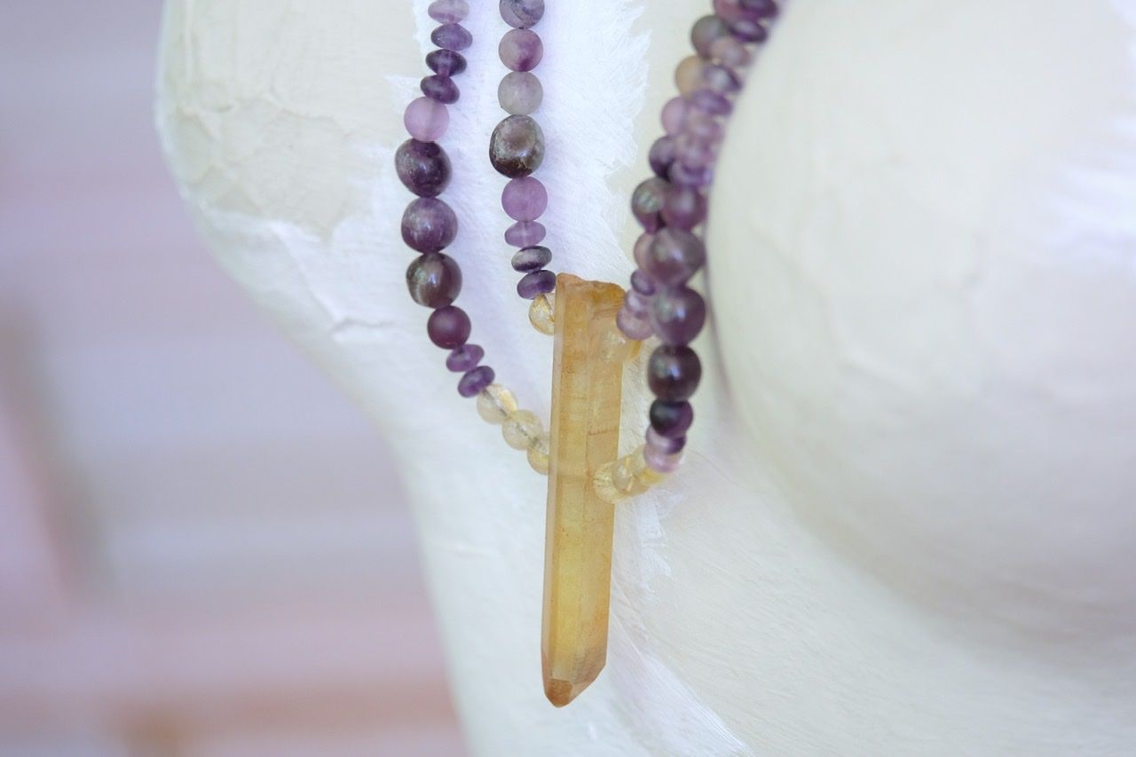 A white mannequin wears a purple and golden yellow stone necklace 