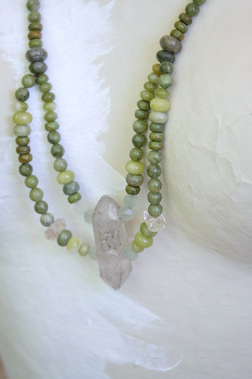 White female form mannequin wearing a crystal and green stone necklace 