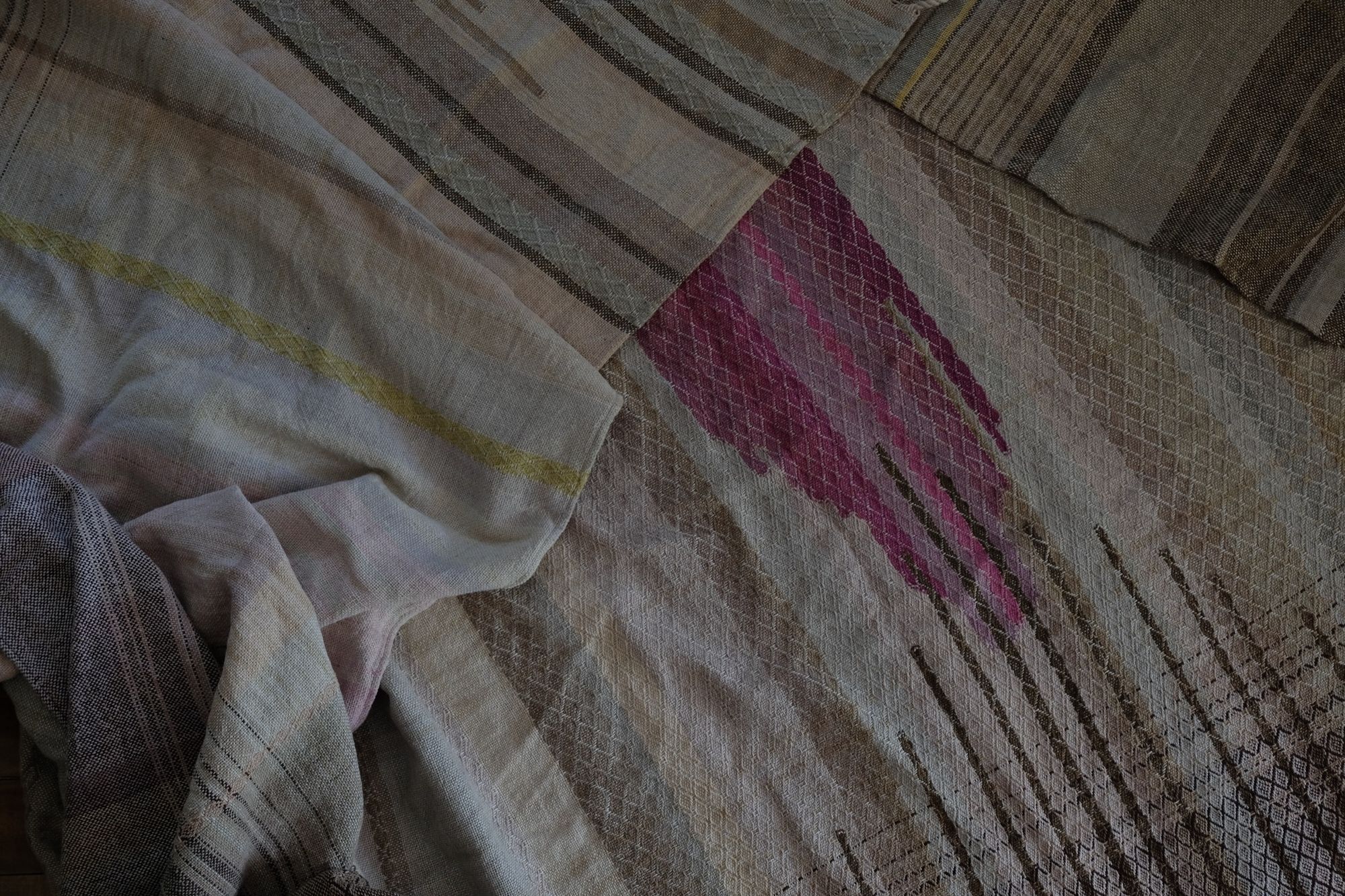 Handwoven fabric in soft shades of grey, pink, yellow and earth laying on a wooden floor