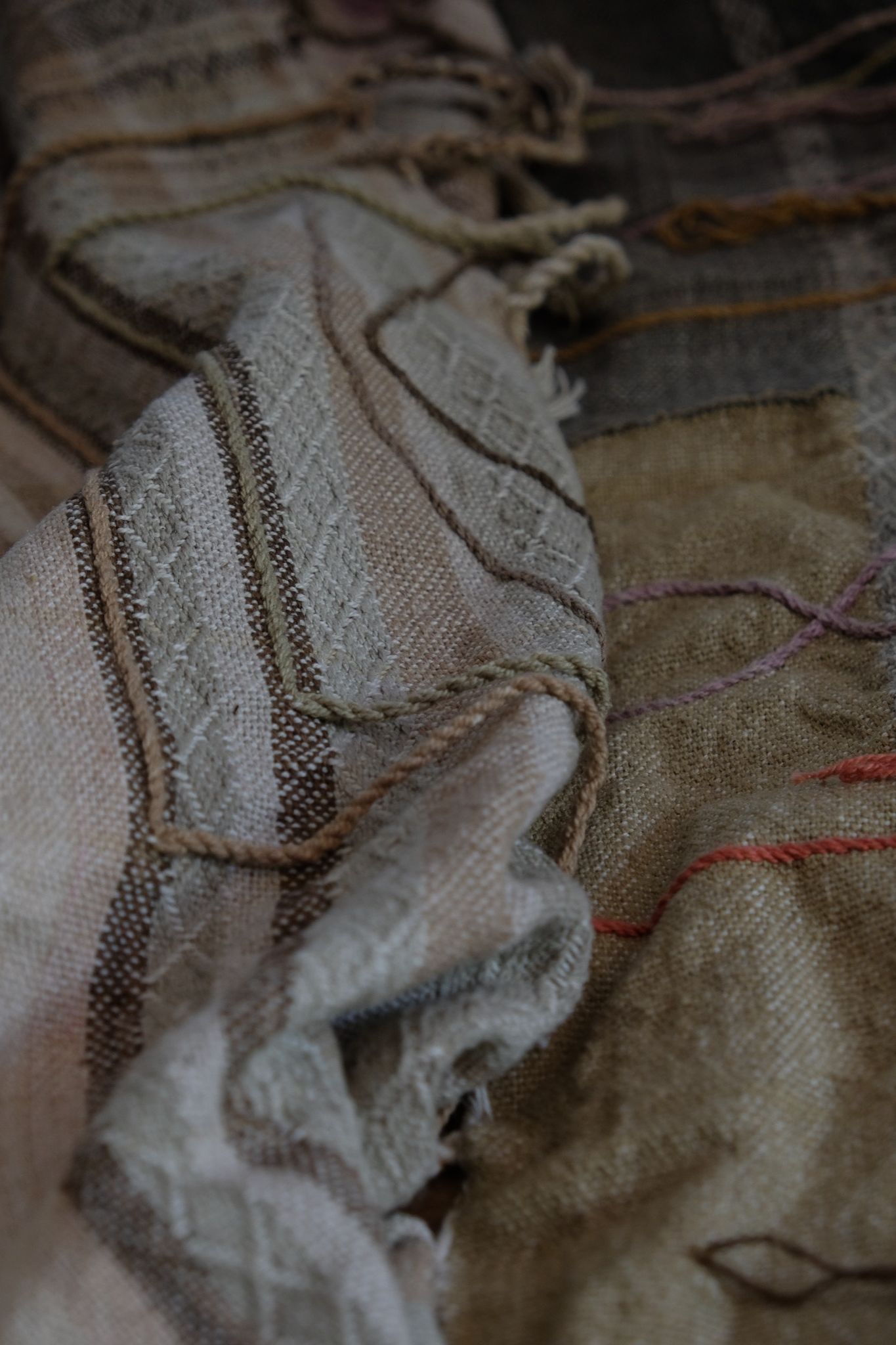 Handwoven fabric in soft shades of grey, pink, yellow and earth laying on a wooden floor