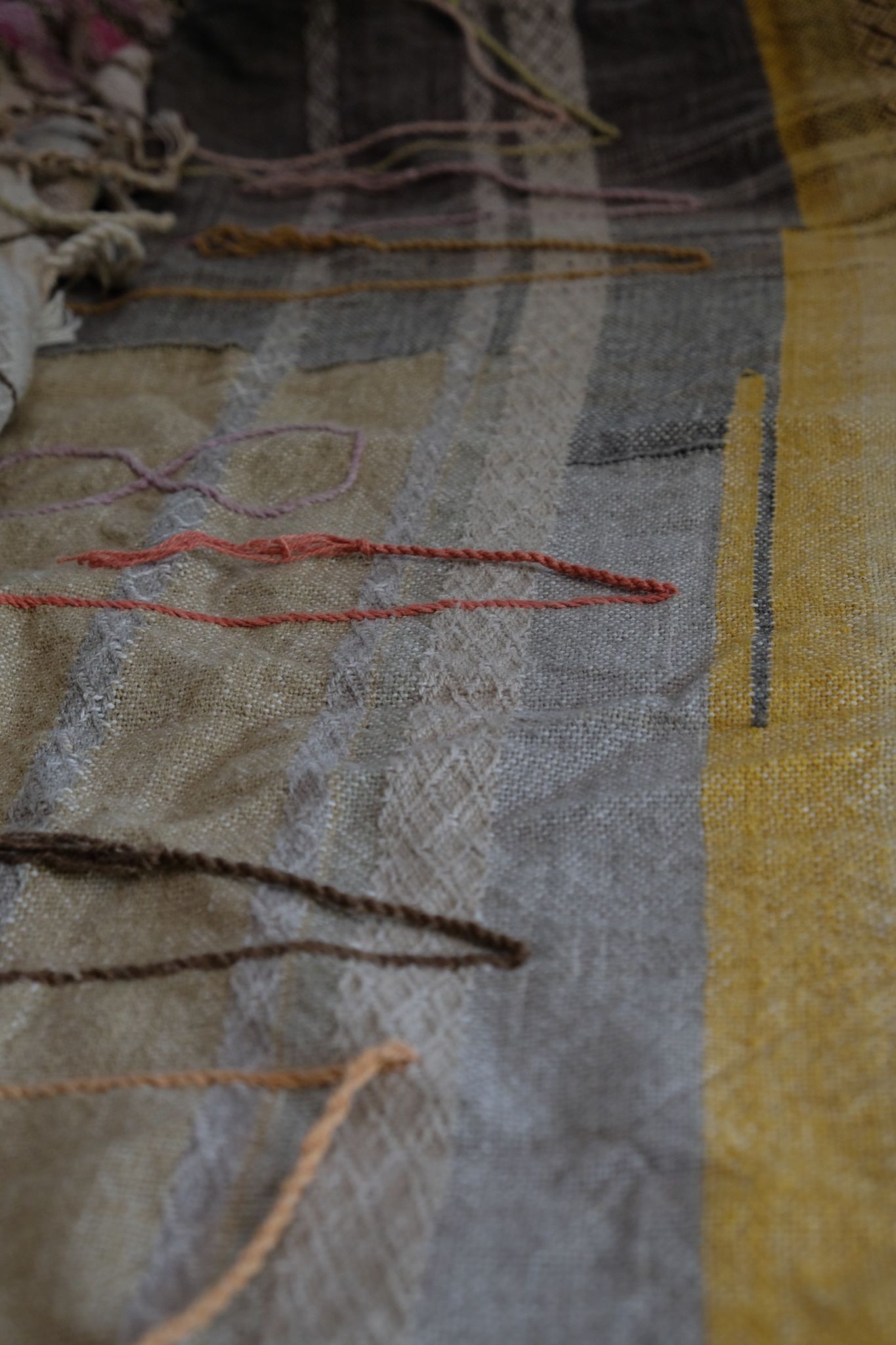 Handwoven fabric in soft shades of grey, pink, yellow and earth laying on a wooden floor