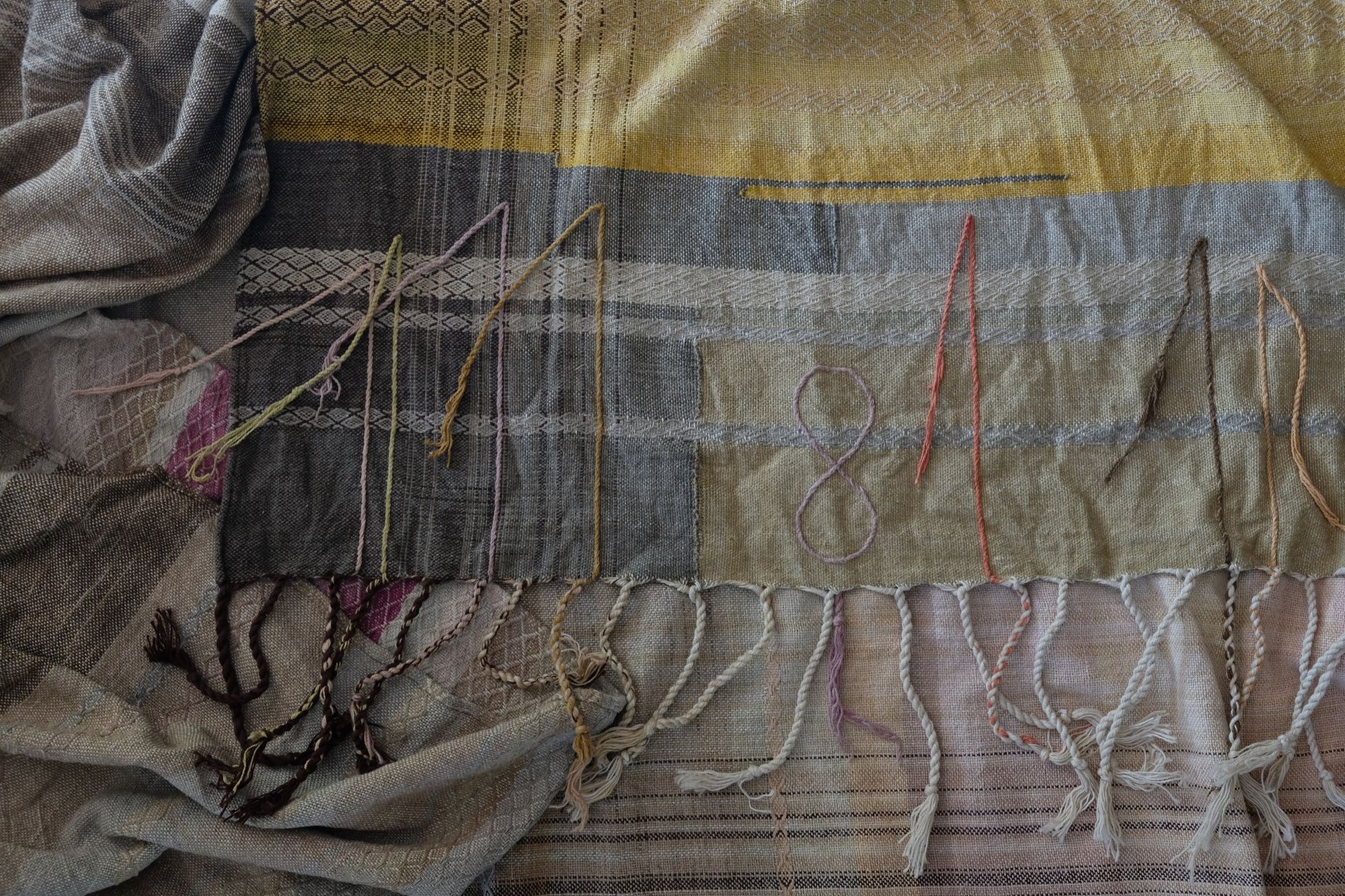 Handwoven fabric in soft shades of grey, pink, yellow and earth laying on a wooden floor