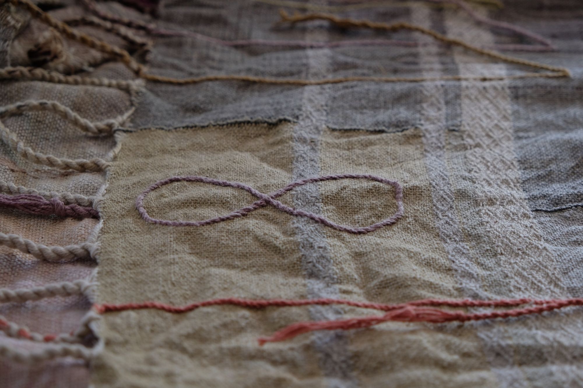 Handwoven fabric in soft shades of grey, pink, yellow and earth laying on a wooden floor