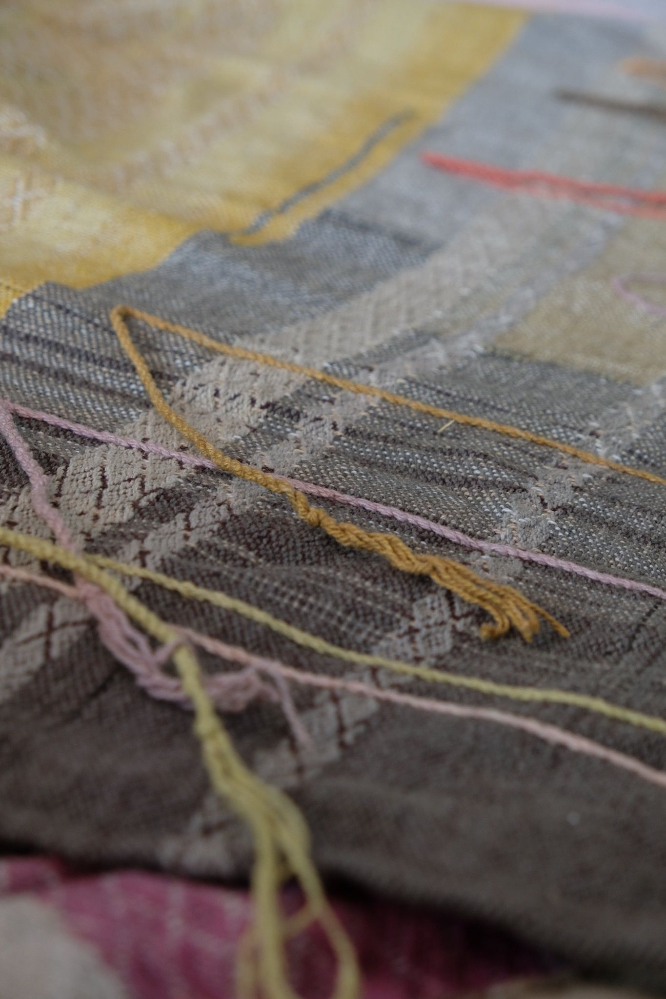 Handwoven fabric in soft shades of grey, pink, yellow and earth laying on a wooden floor