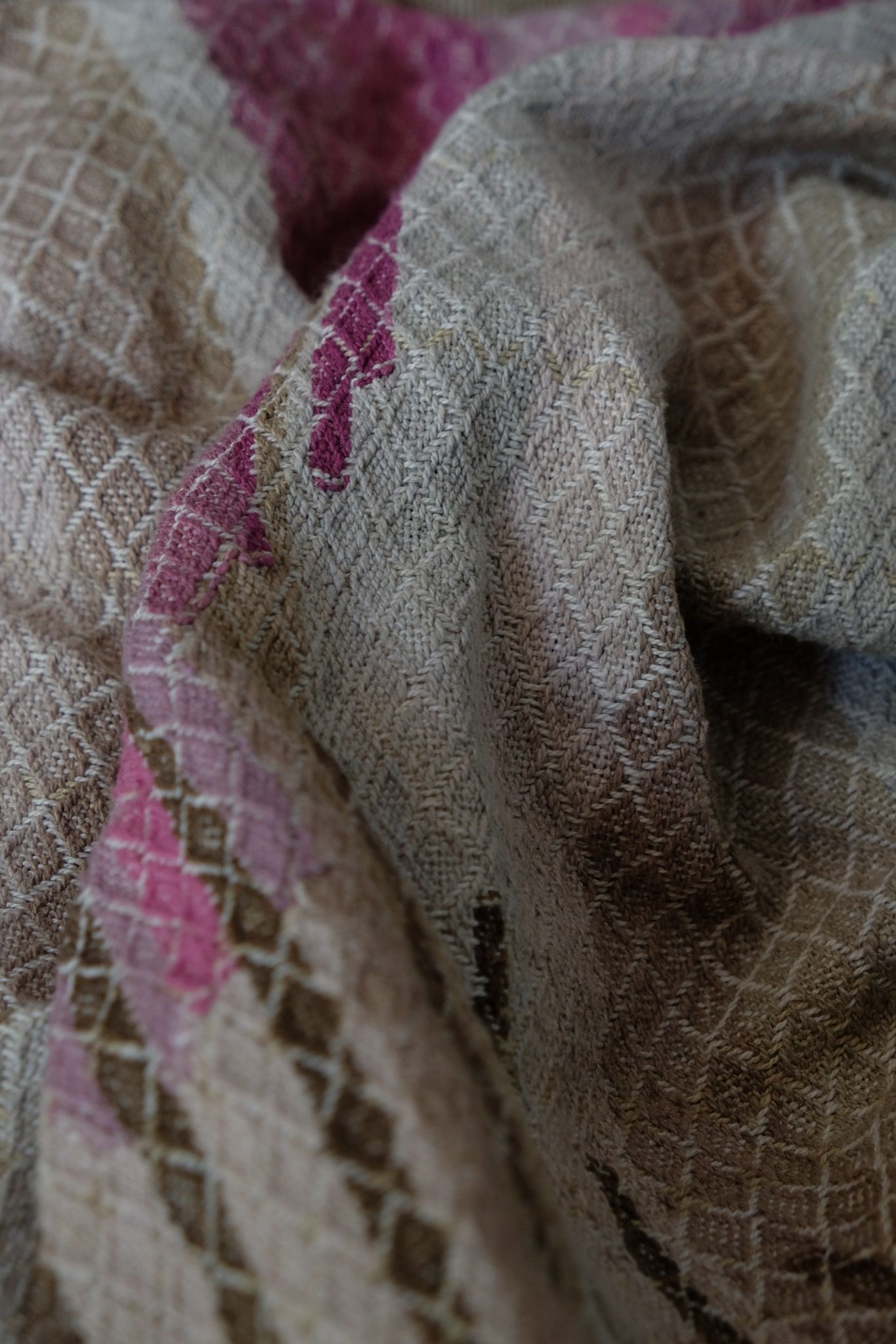 Handwoven fabric in soft shades of grey, pink, yellow and earth laying on a wooden floor