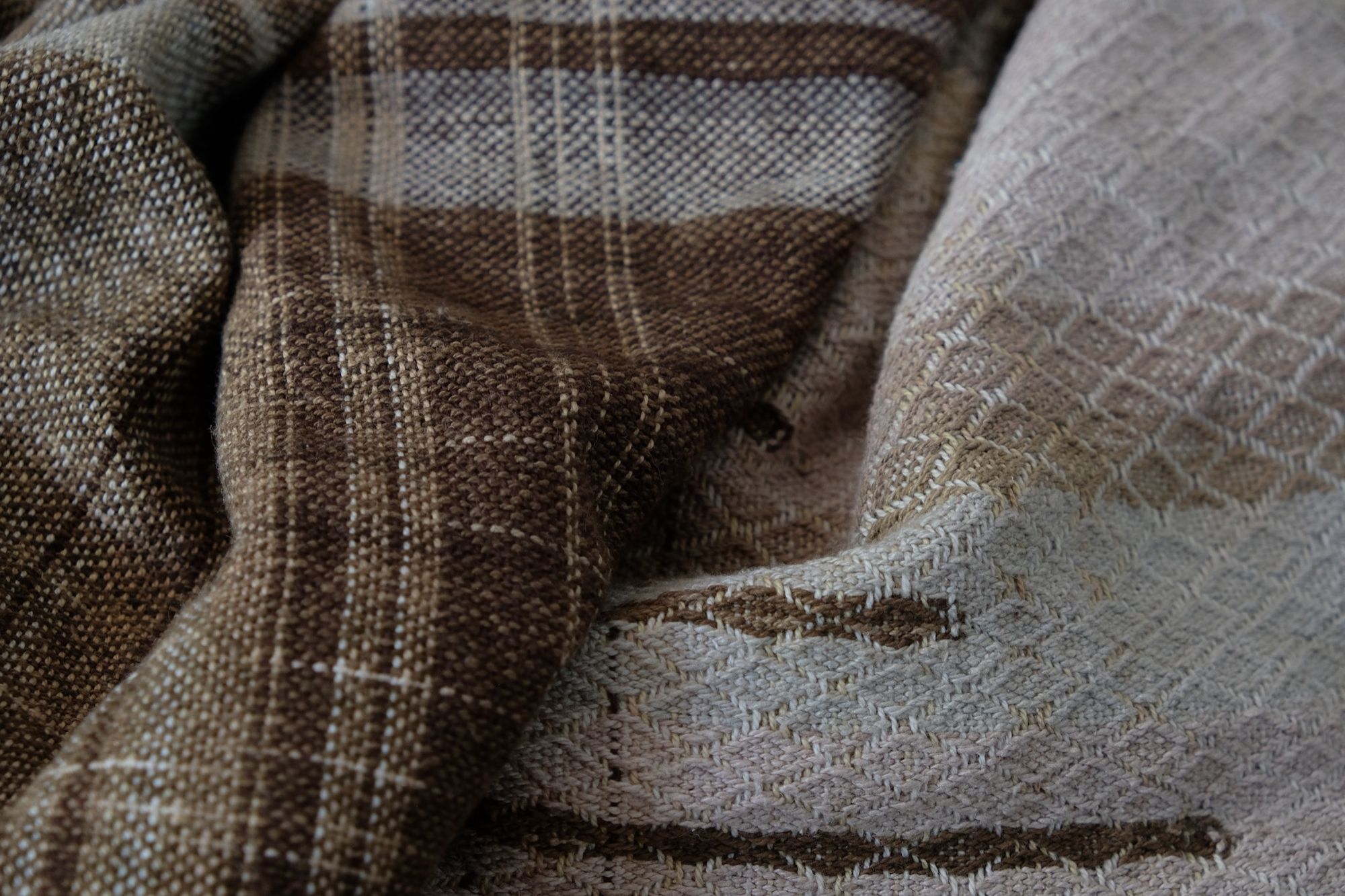 Handwoven fabric in soft shades of grey, pink, yellow and earth laying on a wooden floor