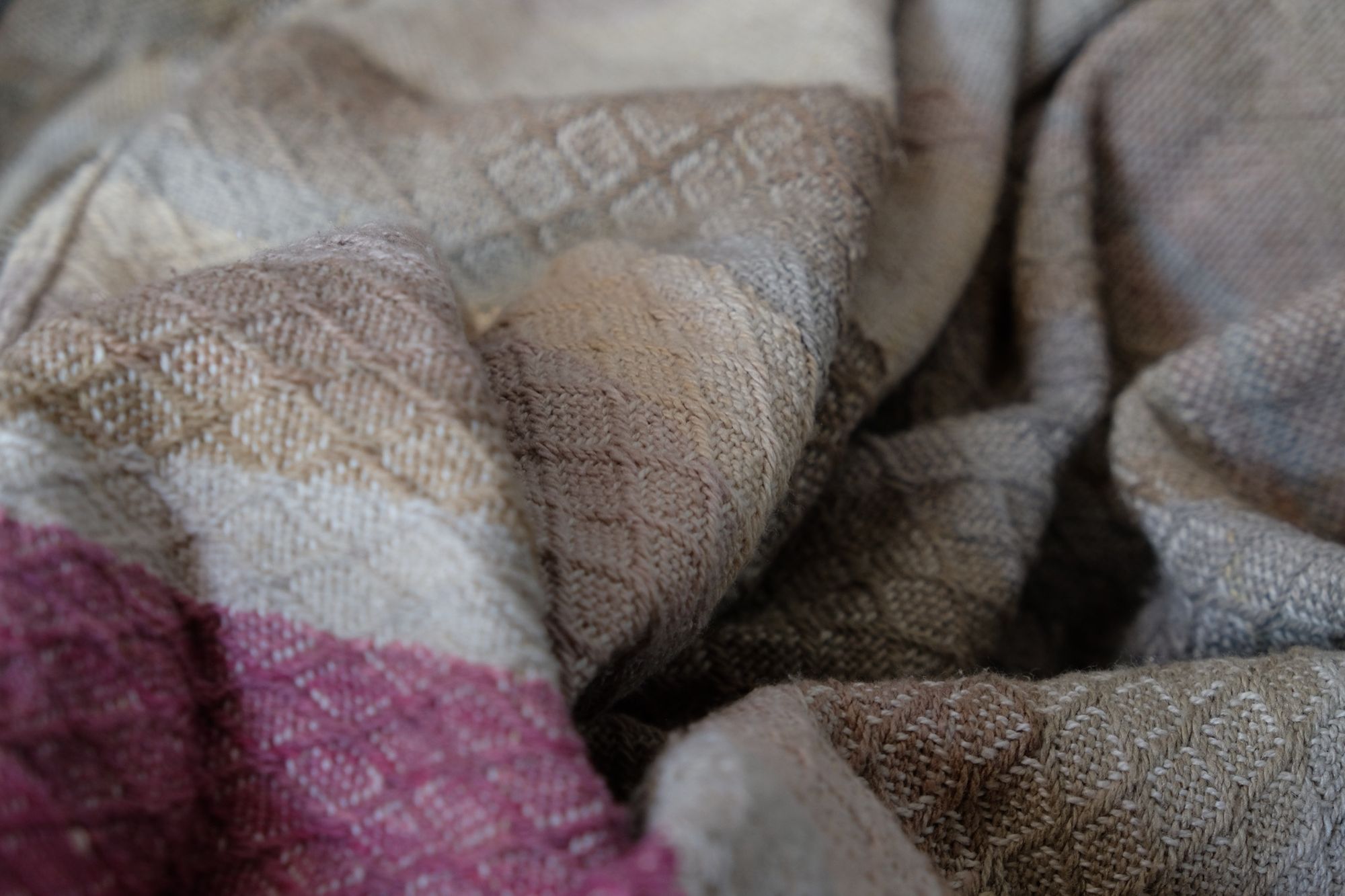 Handwoven fabric in soft shades of grey, pink, yellow and earth laying on a wooden floor