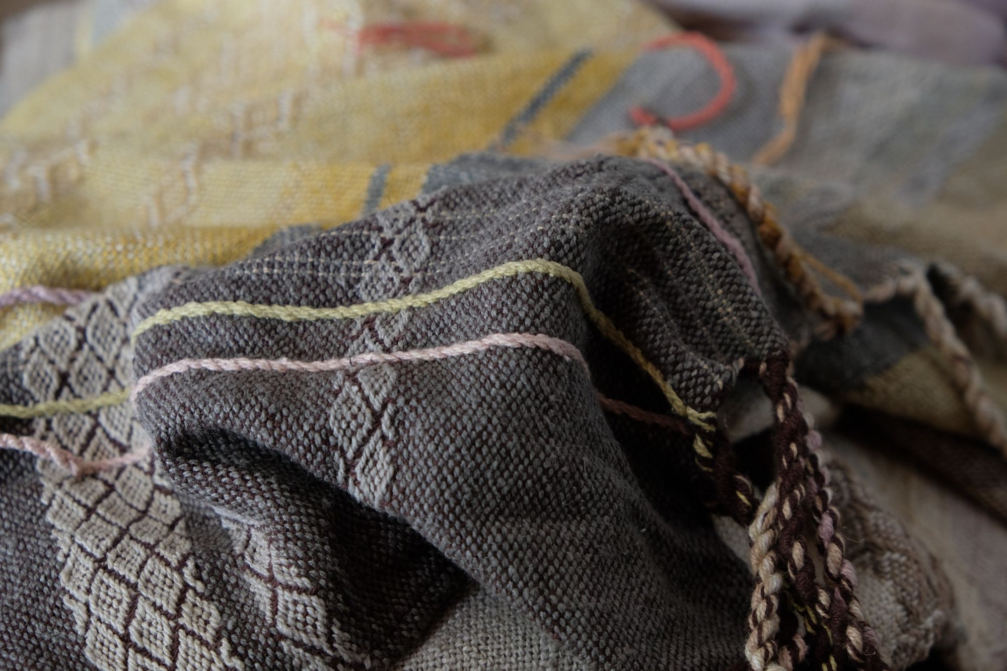 Handwoven fabric in soft shades of grey, pink, yellow and earth laying on a wooden floor