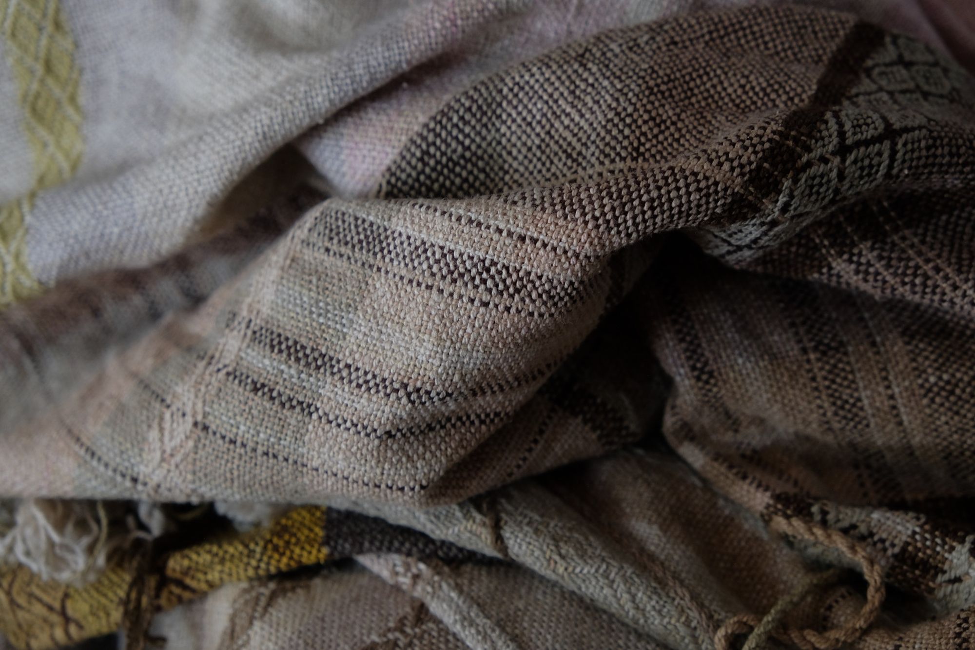 Handwoven fabric in soft shades of grey, pink, yellow and earth laying on a wooden floor