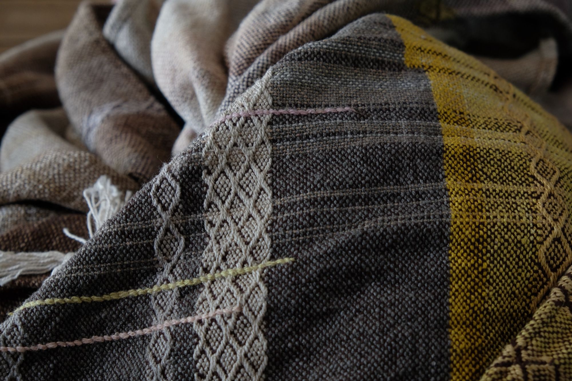 Handwoven fabric in soft shades of grey, pink, yellow and earth laying on a wooden floor