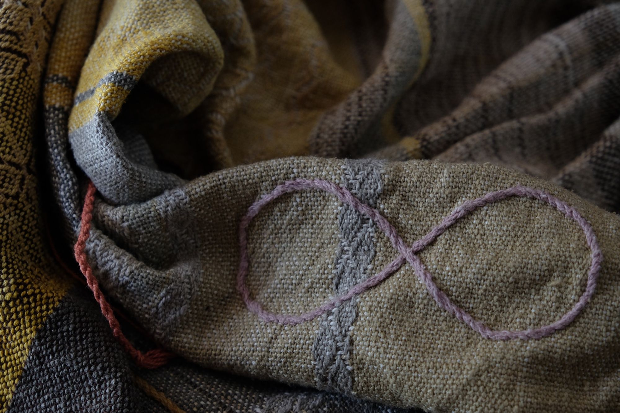 Handwoven fabric in soft shades of grey, pink, yellow and earth laying on a wooden floor