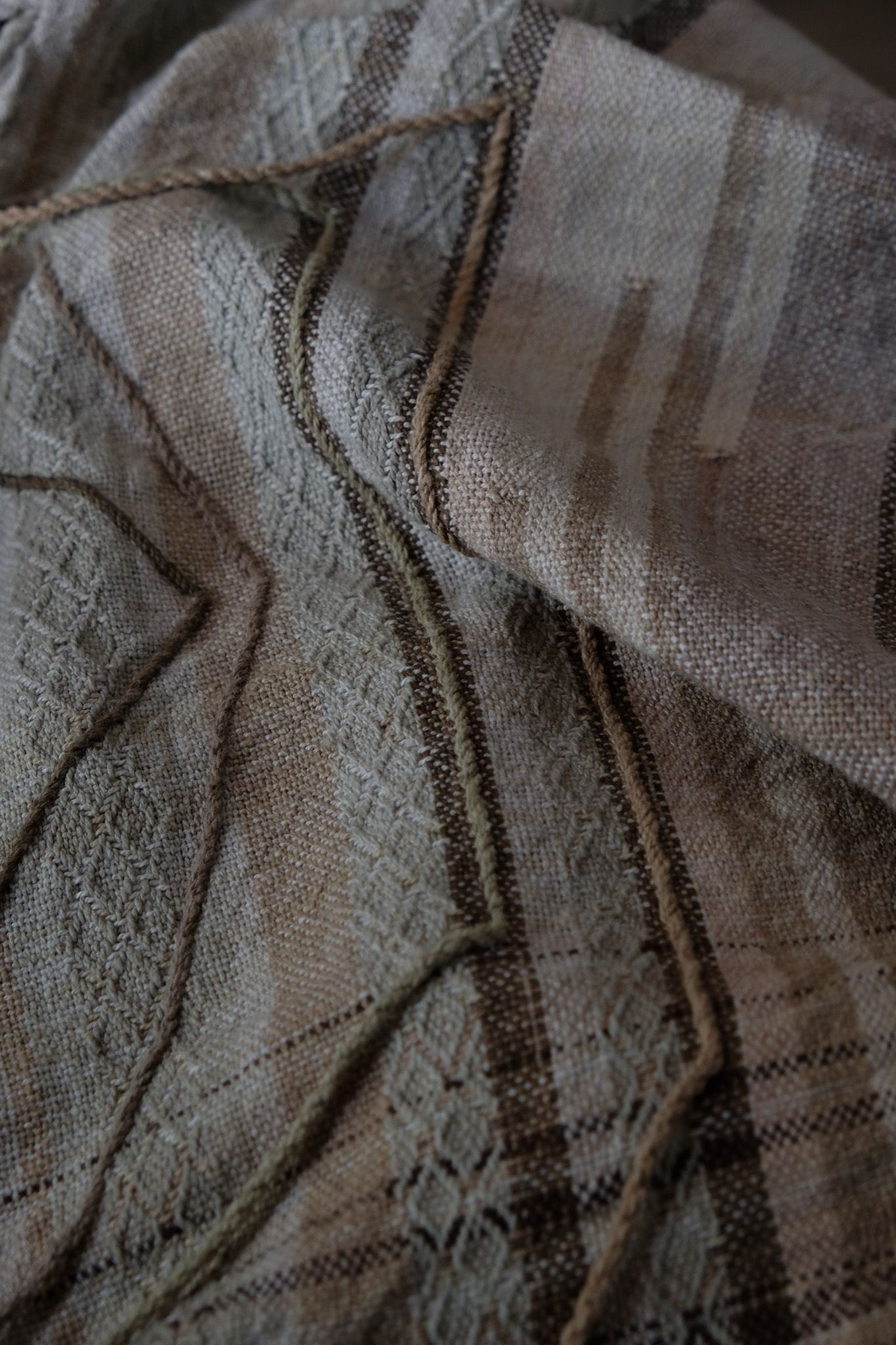 Handwoven fabric in soft shades of grey, pink, yellow and earth laying on a wooden floor