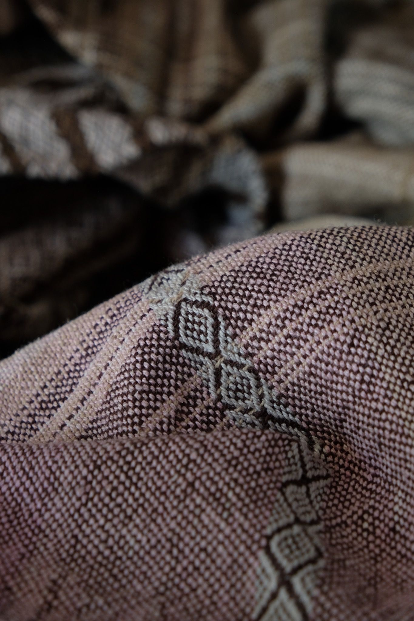 Handwoven fabric in soft shades of grey, pink, yellow and earth laying on a wooden floor