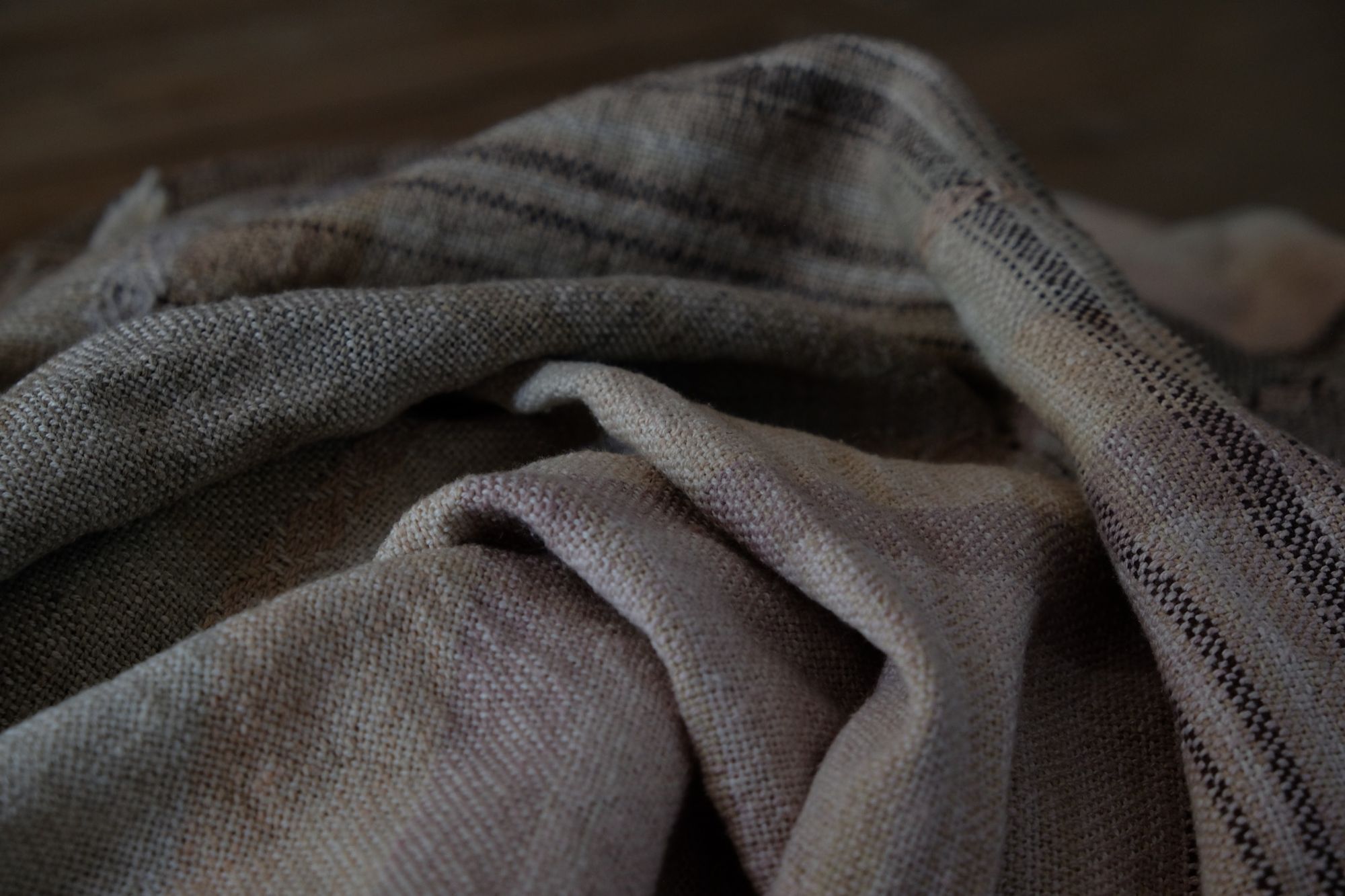 Handwoven fabric in soft shades of grey, pink, yellow and earth laying on a wooden floor