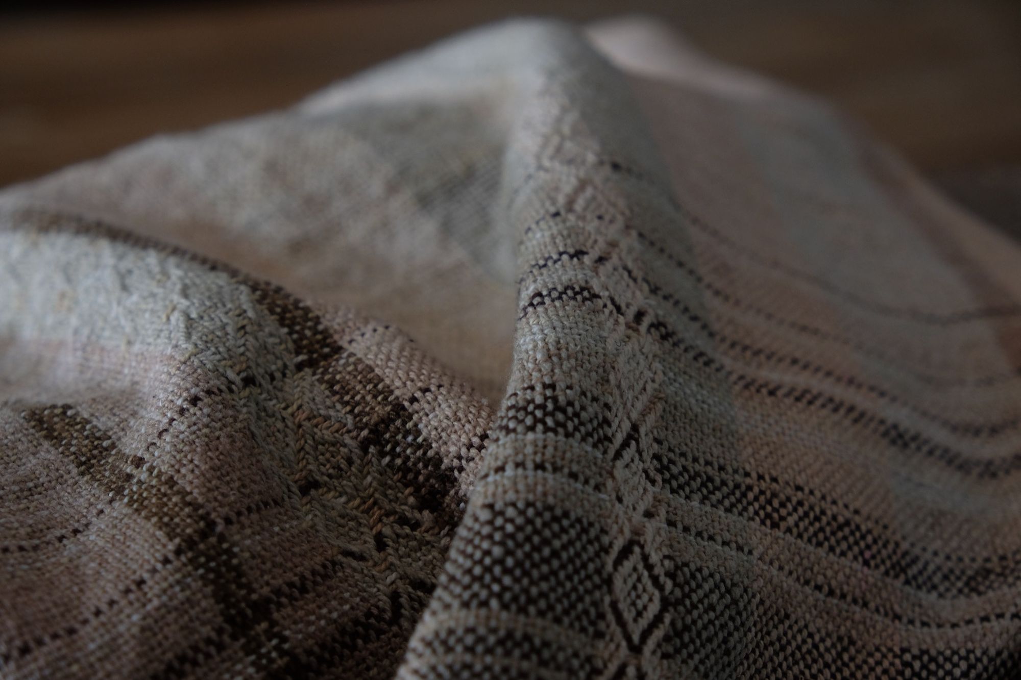 Handwoven fabric in soft shades of grey, pink, yellow and earth laying on a wooden floor