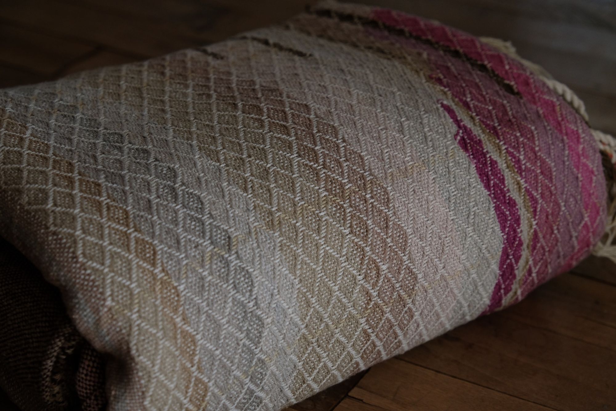 Handwoven fabric in soft shades of grey, pink, yellow and earth laying on a wooden floor