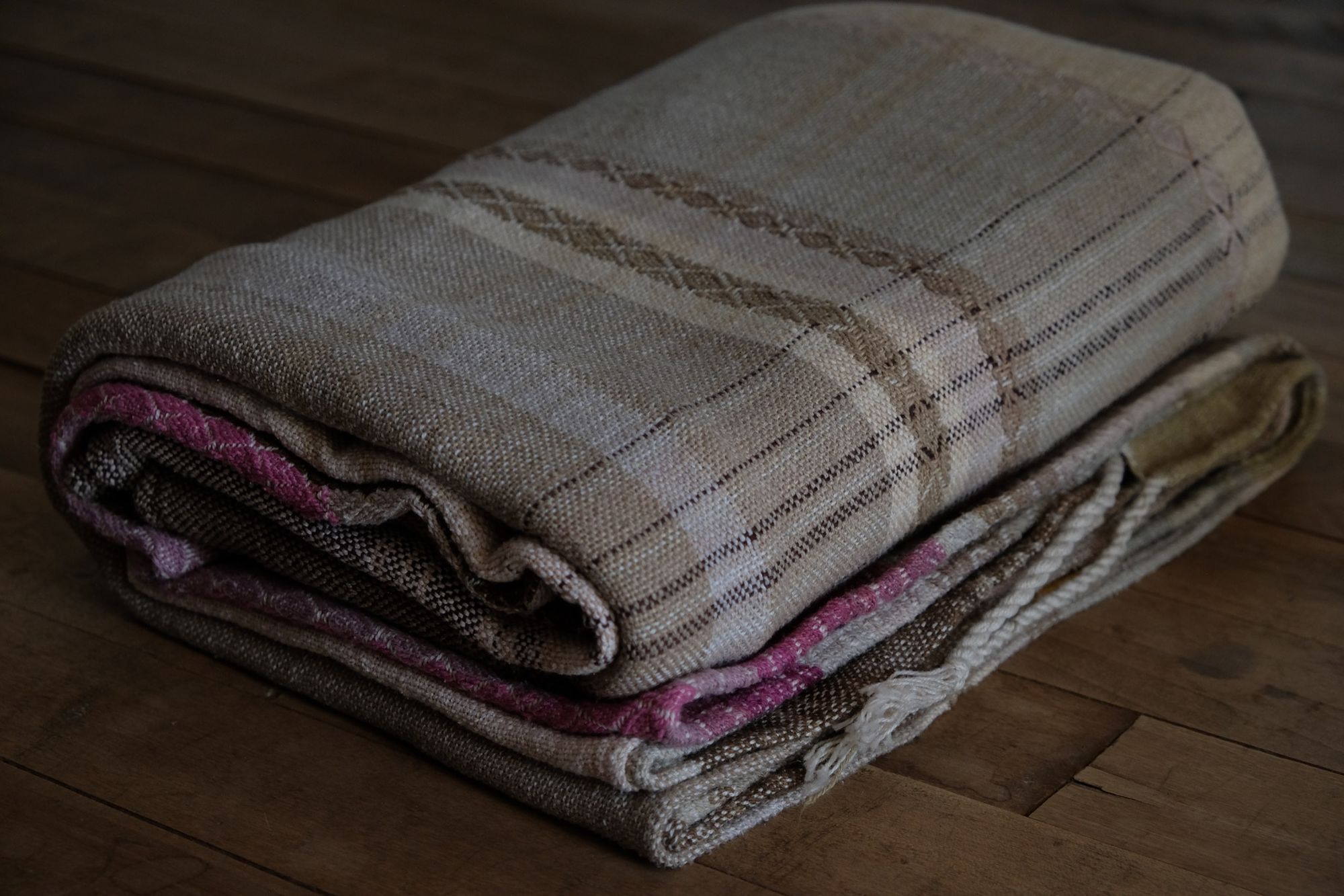 Handwoven fabric in soft shades of grey, pink, yellow and earth laying on a wooden floor